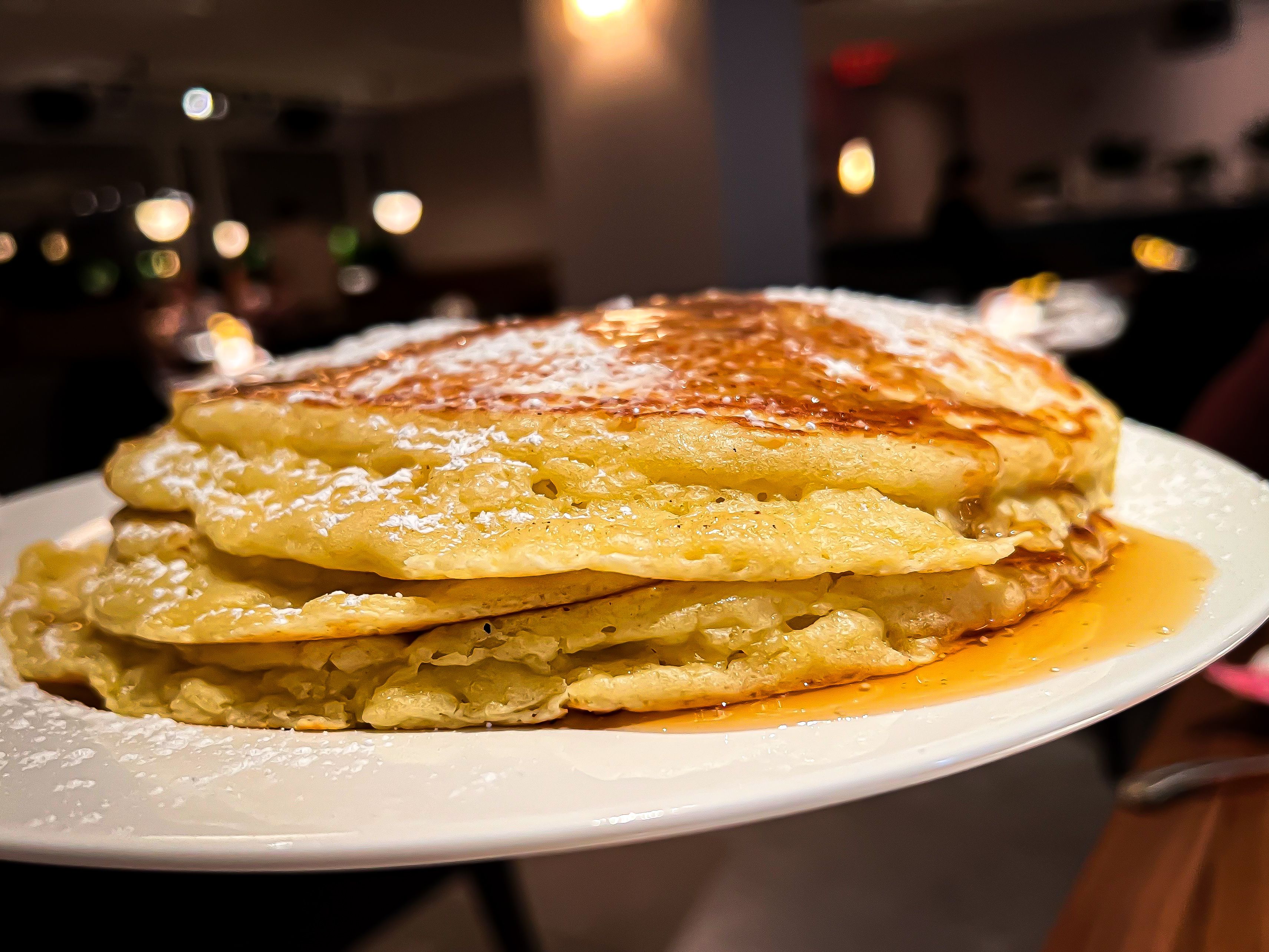 A stack of pancakes with powdered sugar and syrup. 
