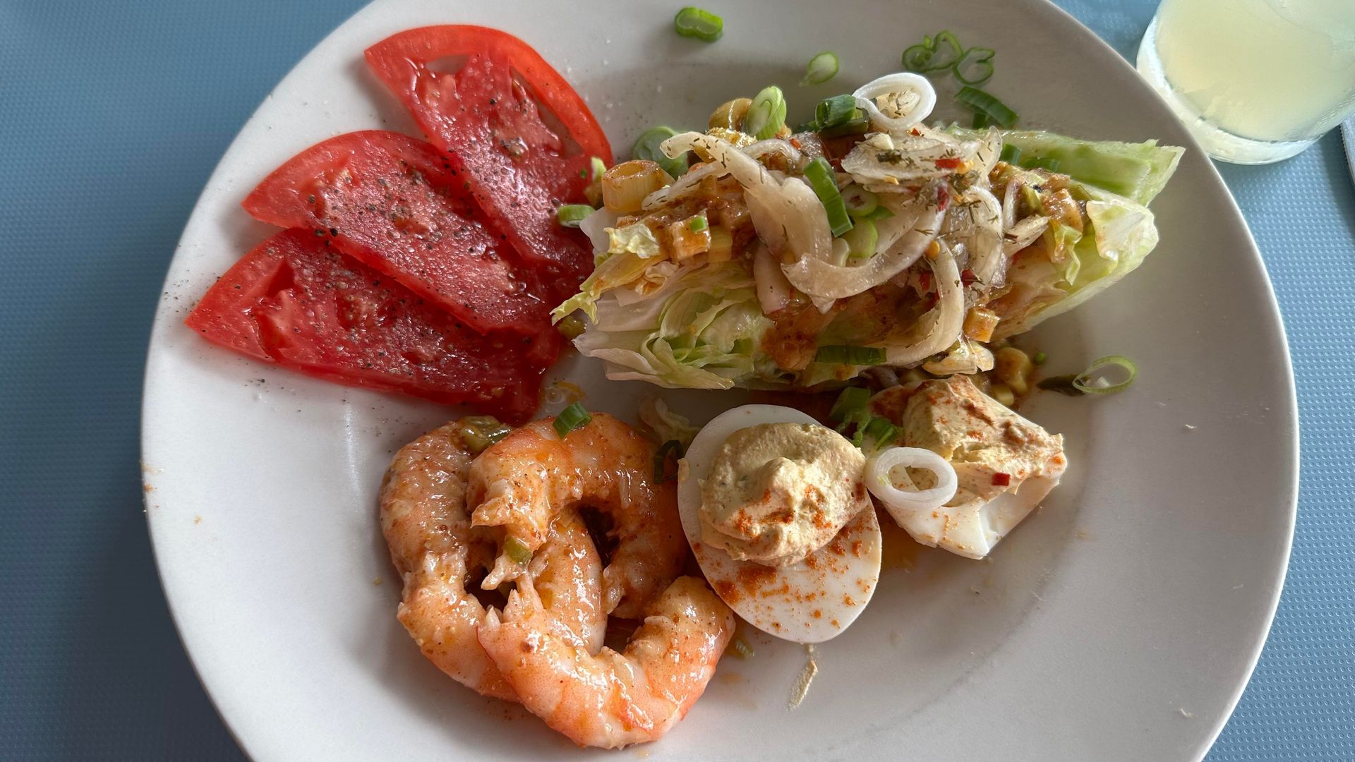 Photo shows a wedge salad with remoulade dressing, deviled eggs, cooked shrimp, sliced tomatoes and a glass of lemonade.