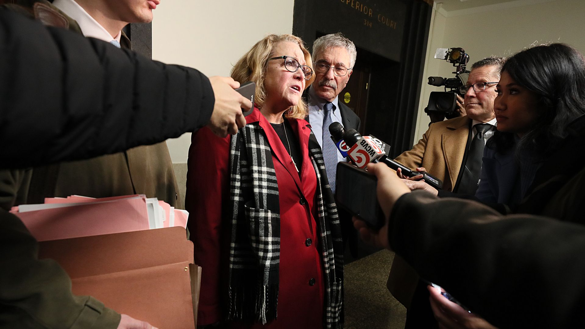 Cannabis Control Commission Chair Shannon O'Brien, center, stands beside her attorney addressing reporters, who are holding up their microphones and recorders. 