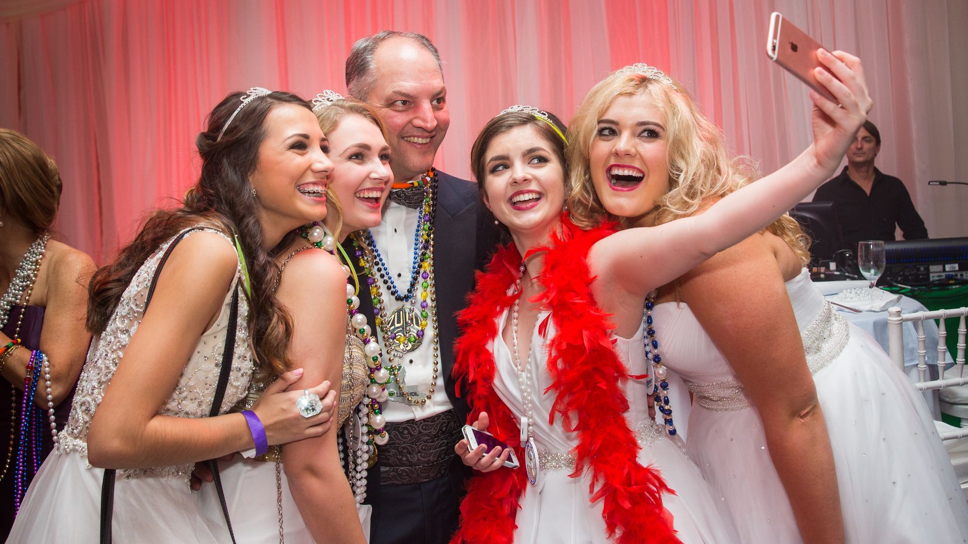 Gov. John Bel Edwards poses for a selfie, standing in the middle of a group of four beauty queens as one holds up a phone to snap a photo.