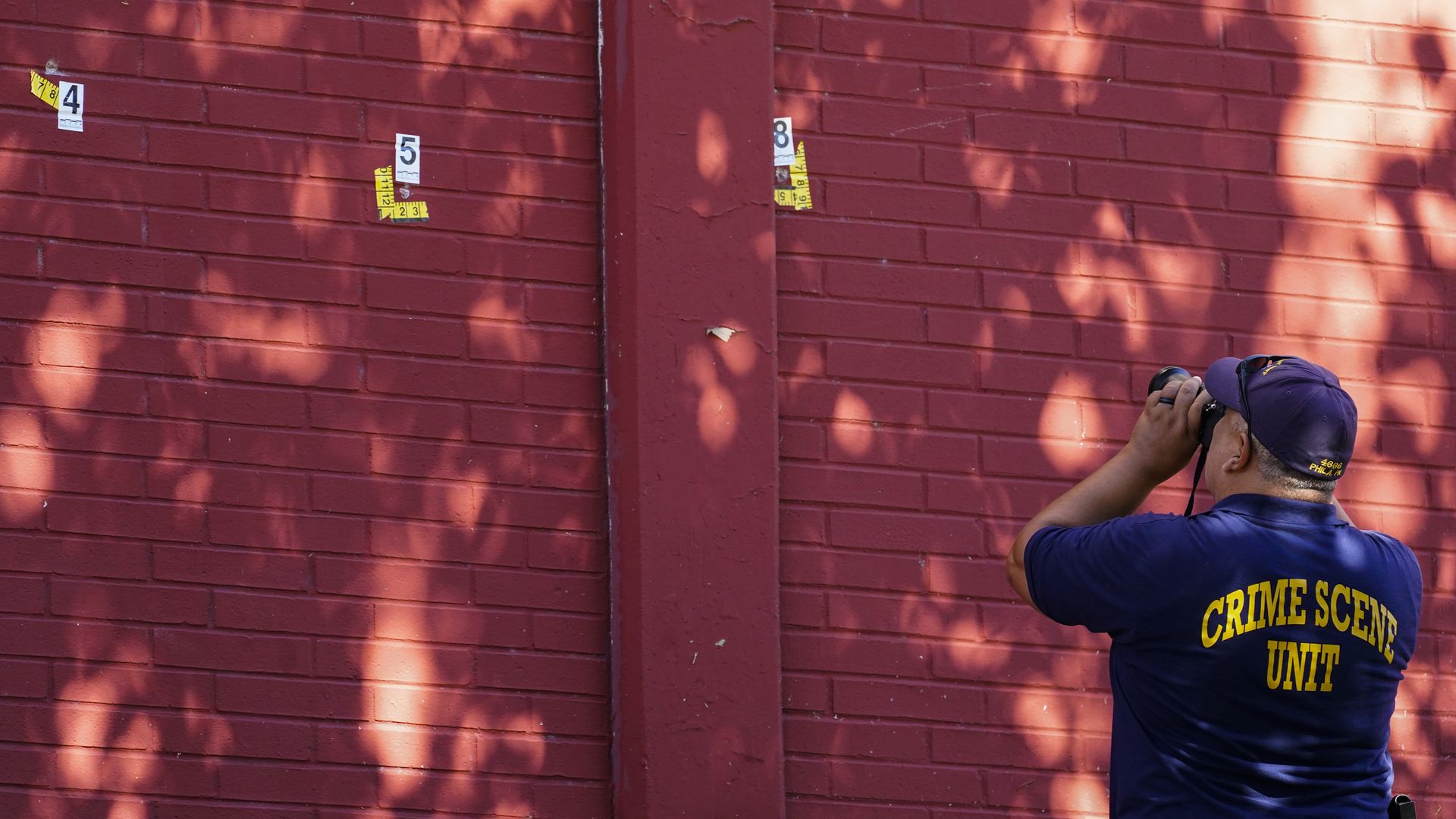 An investigator takes photos of a wall where bullets struck it. 