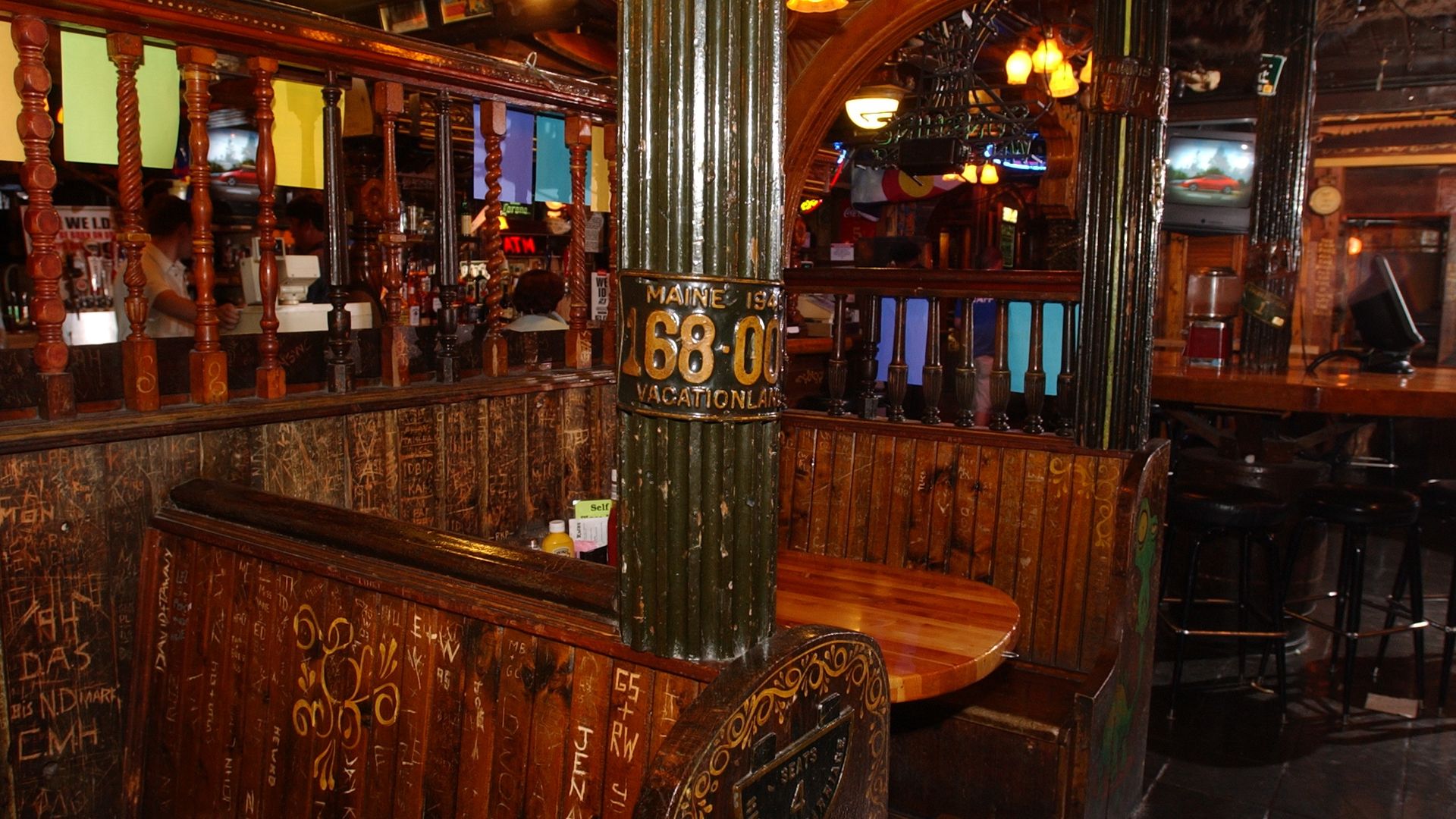 Inside the Dark Horse: Cozy wooden booth seating inside a dimly lit bar with carved graffiti on the wood, a dark green pillar with a Maine vacationland sign, and warm yellow and orange hanging lights.