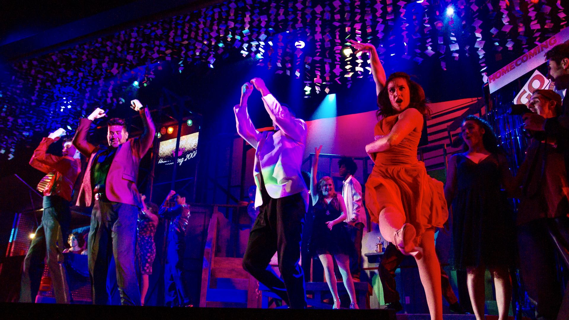 Actors are shown dancing on a stage during a musical performance of the show Americano