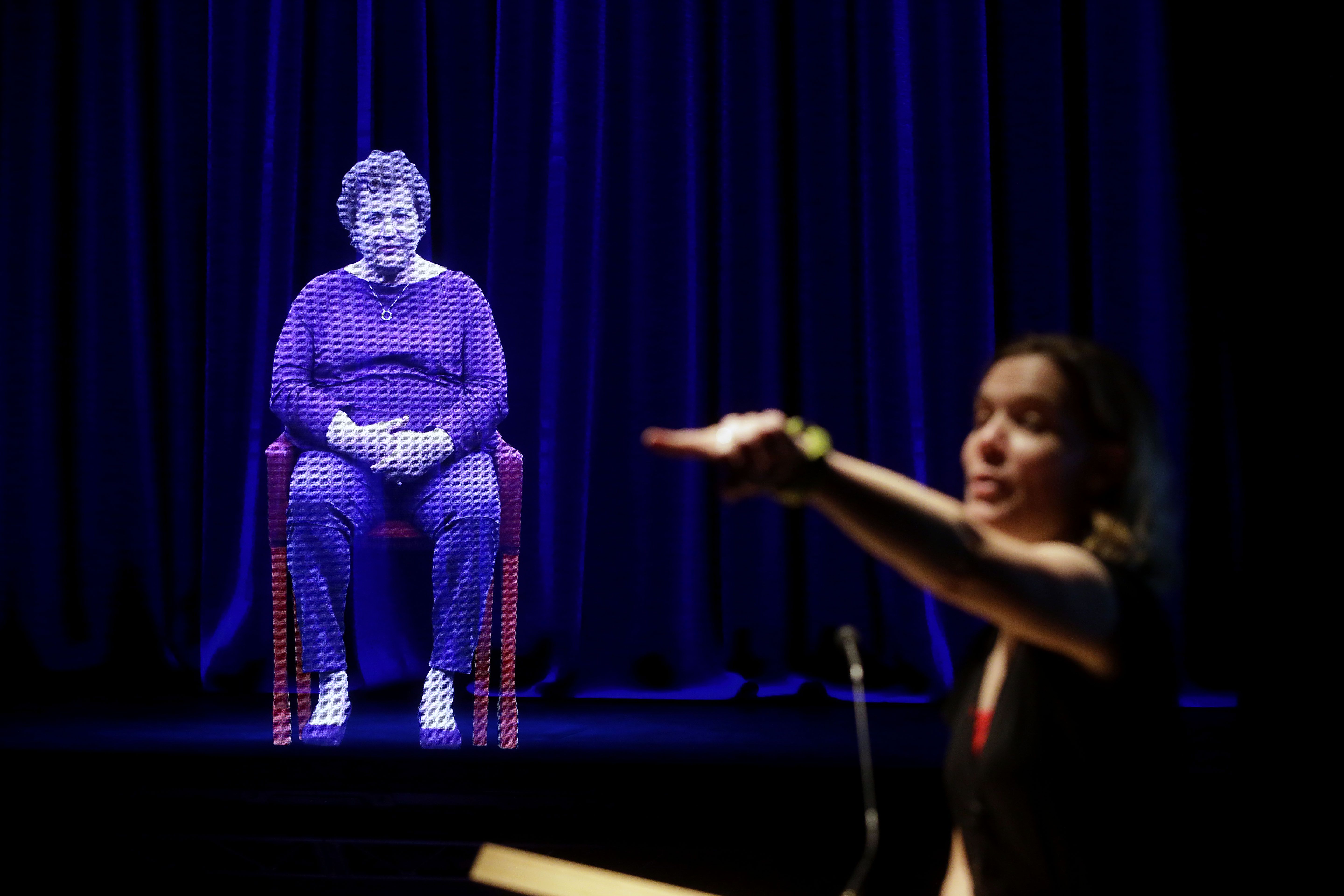 A holographic image of a Holocaust survivor is displayed on a stage.