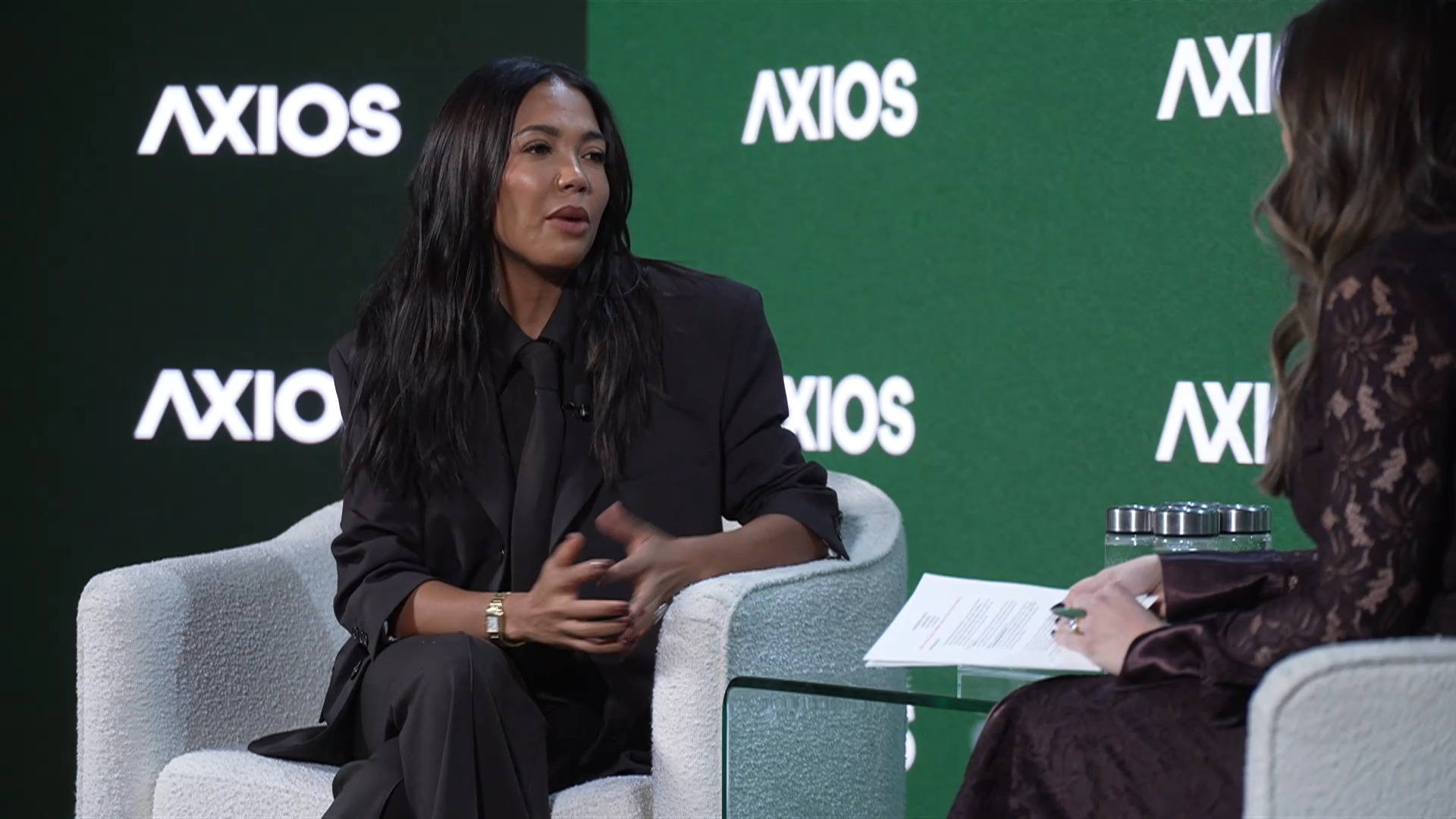 Grede wearing a full black outfit in front of an Axios banner