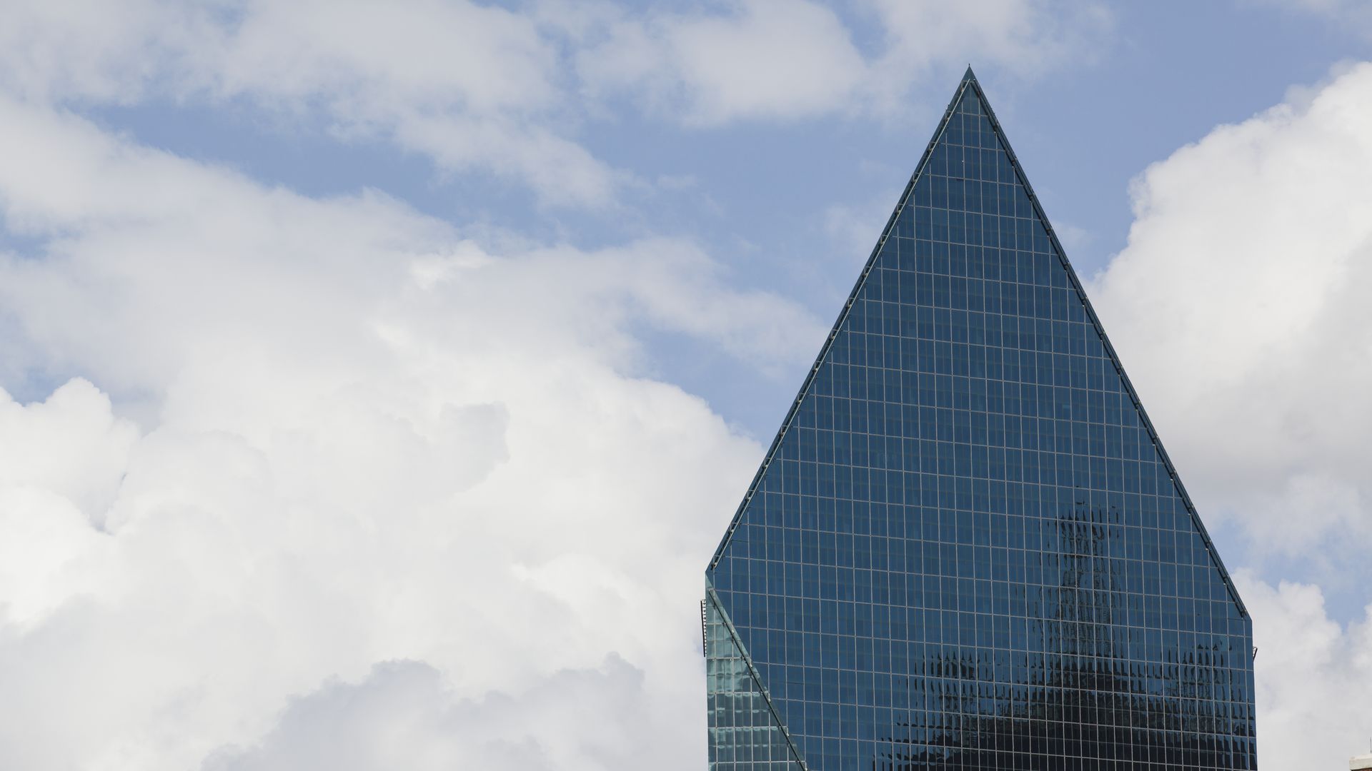 Fountain Place — a sharp, triangular glass skyscraper reflecting clouds against a partly cloudy blue sky — is the fifth tallest skyscraper in Dallas.