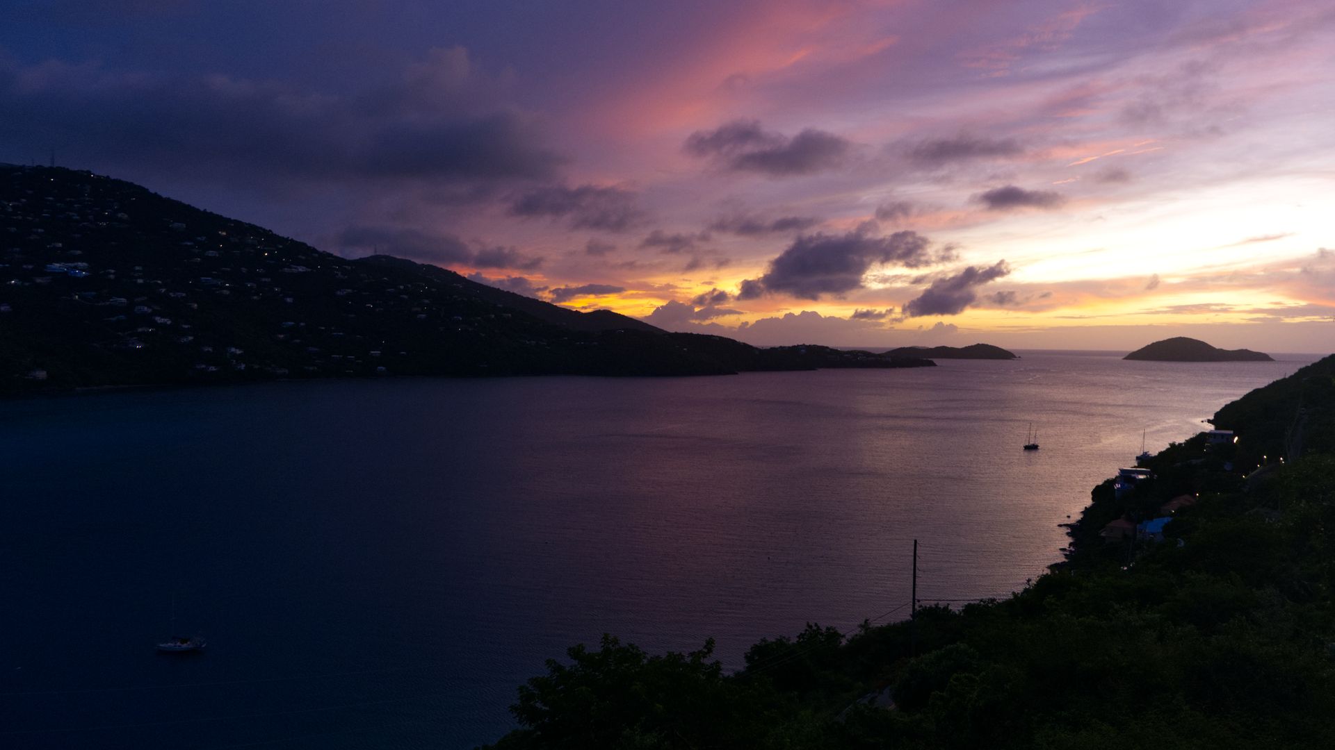 A vibrant sunset on a tropical island. A bay is seen in the middle of the frame, flanked by two pieces of land.