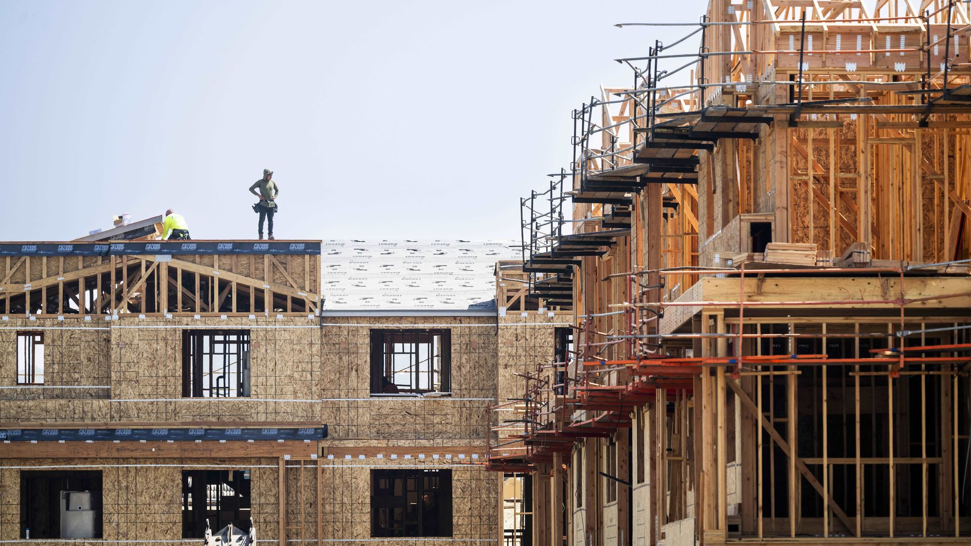 A housing complex under construction with a worker standing on a roof looking at the project.