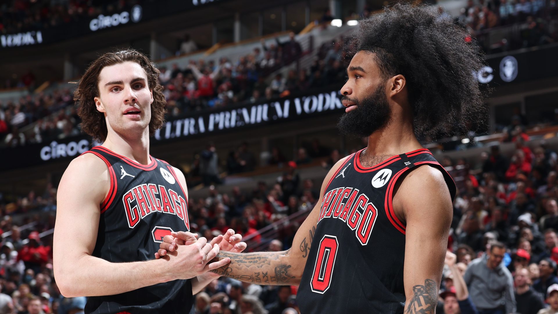 Photo of two basketball players shaking hands on a court in a stadium.