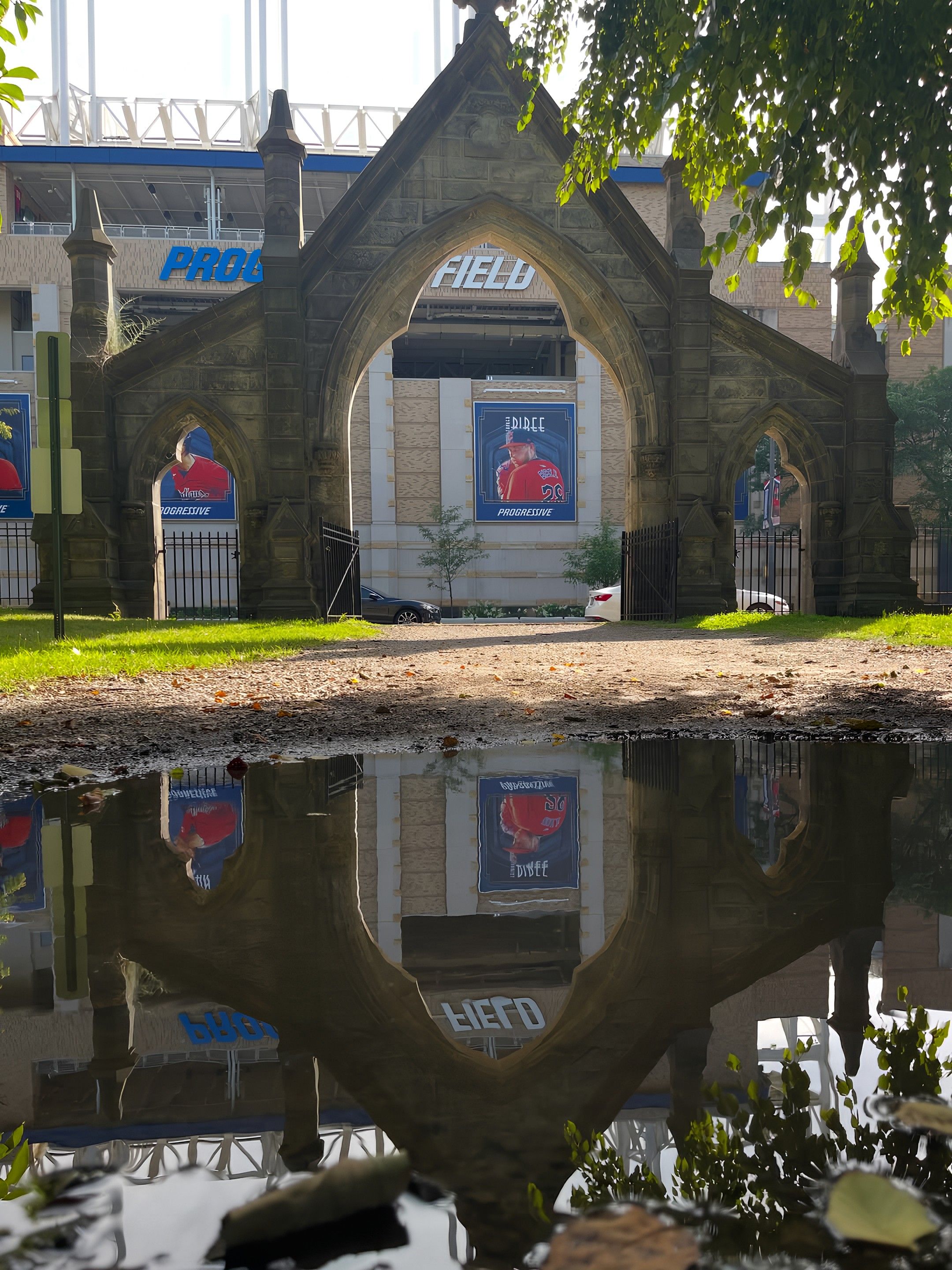 Stone Gothic arch gateway to Progressive Field with three arches; banners of players hang in back; a puddle in the foreground mirrors the arch and scene.