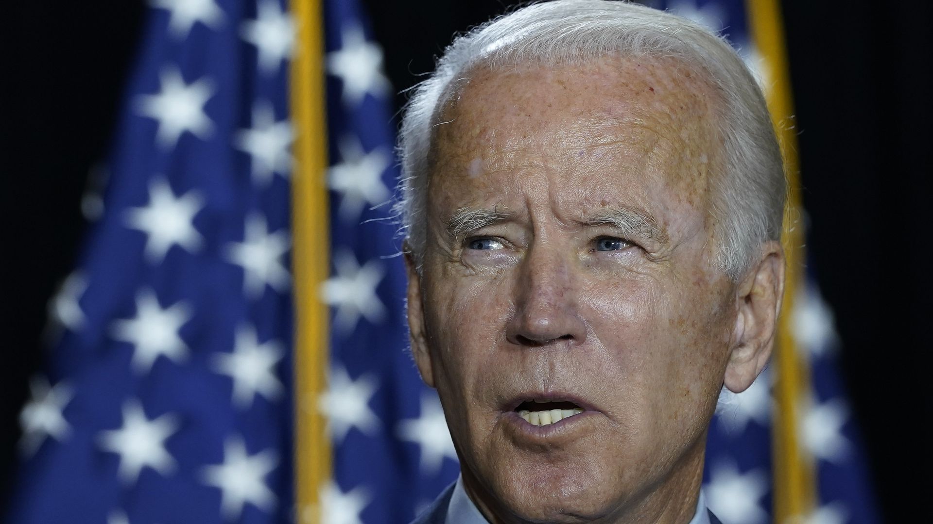 Joe Biden speaks in front of a set of American flags