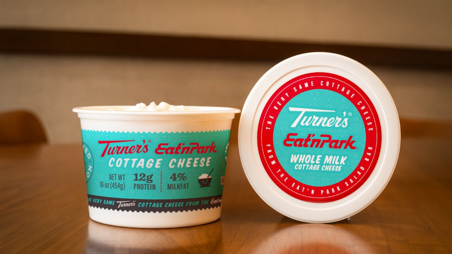 Two containers of Turner's Eat'n Park cottage cheese on a wooden table, one open showing the cheese, labeled 16 oz, 12g protein, 4% milk fat, with teal and red labels.