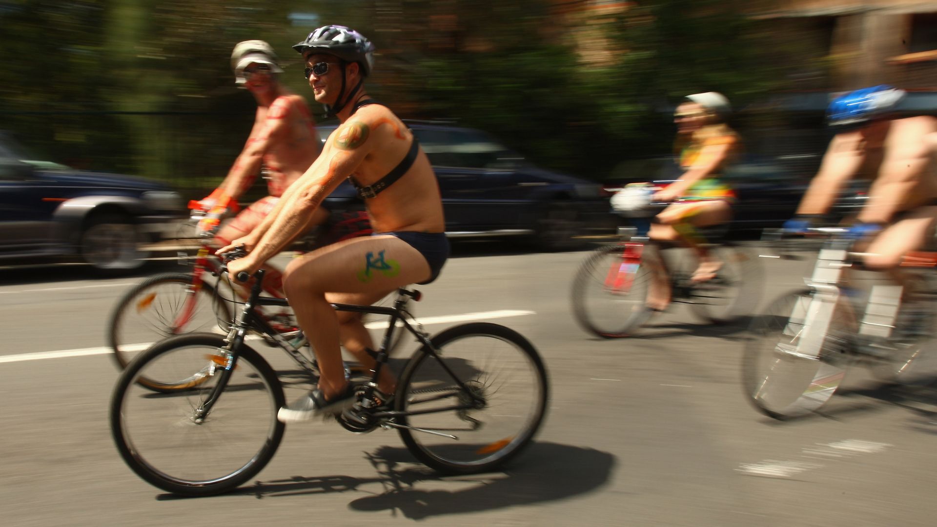 A group of naked bicycle riders pedal quickly along a street