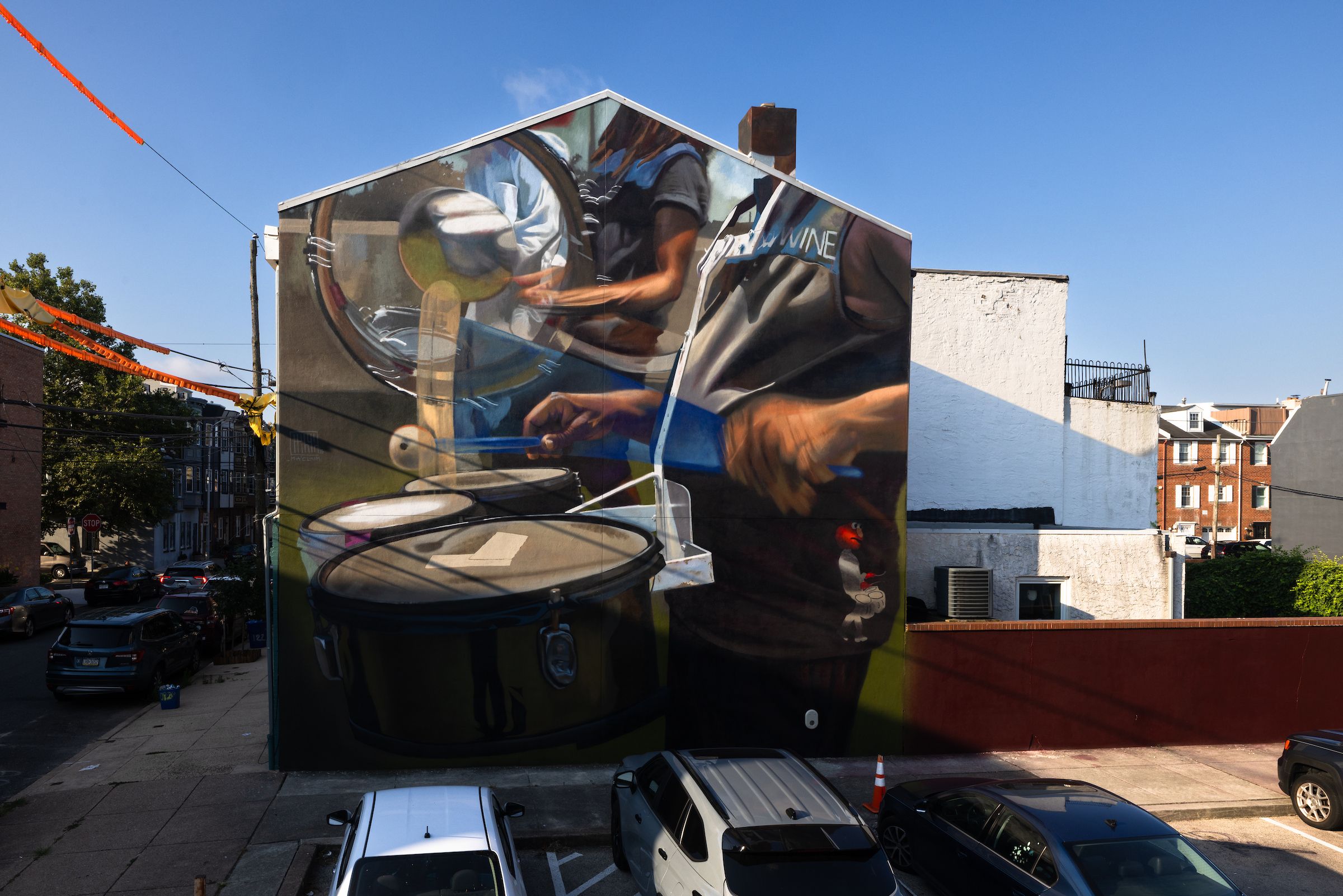 Large mural on building side showing close-up of person playing drums with mallets under a clear blue sky.