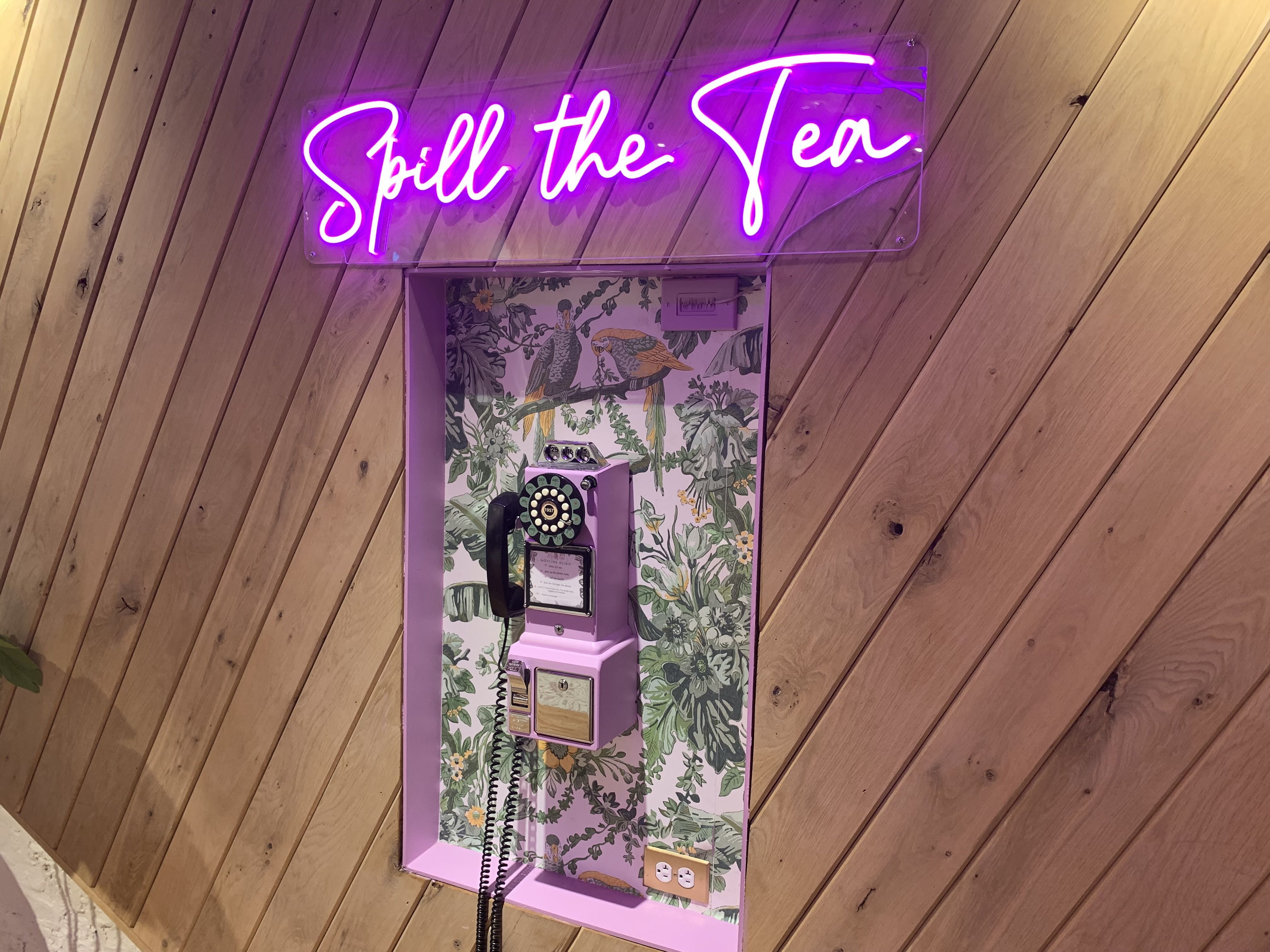 Photo of a phone booth with a neon sign that says "Spill the Tea" 