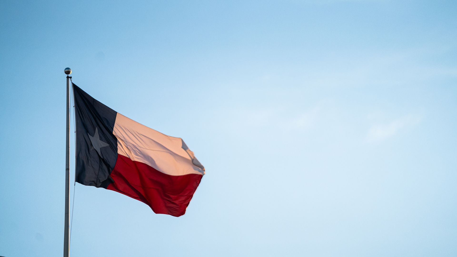 A Texas flag waves in a baby blue sky