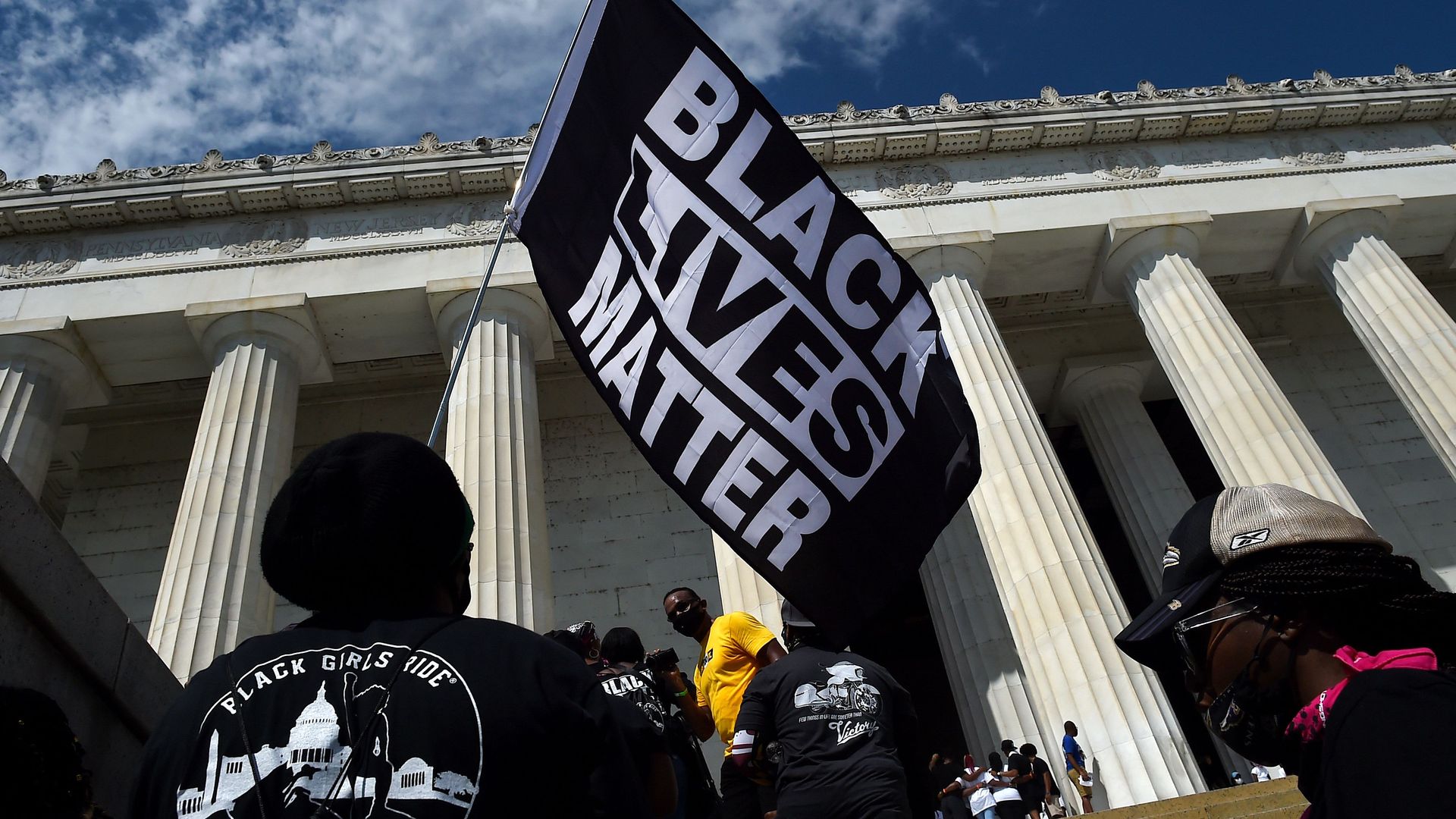 Photo of a person holding a Black Lives Matter flag at a protest in front of the Lincoln Memorial