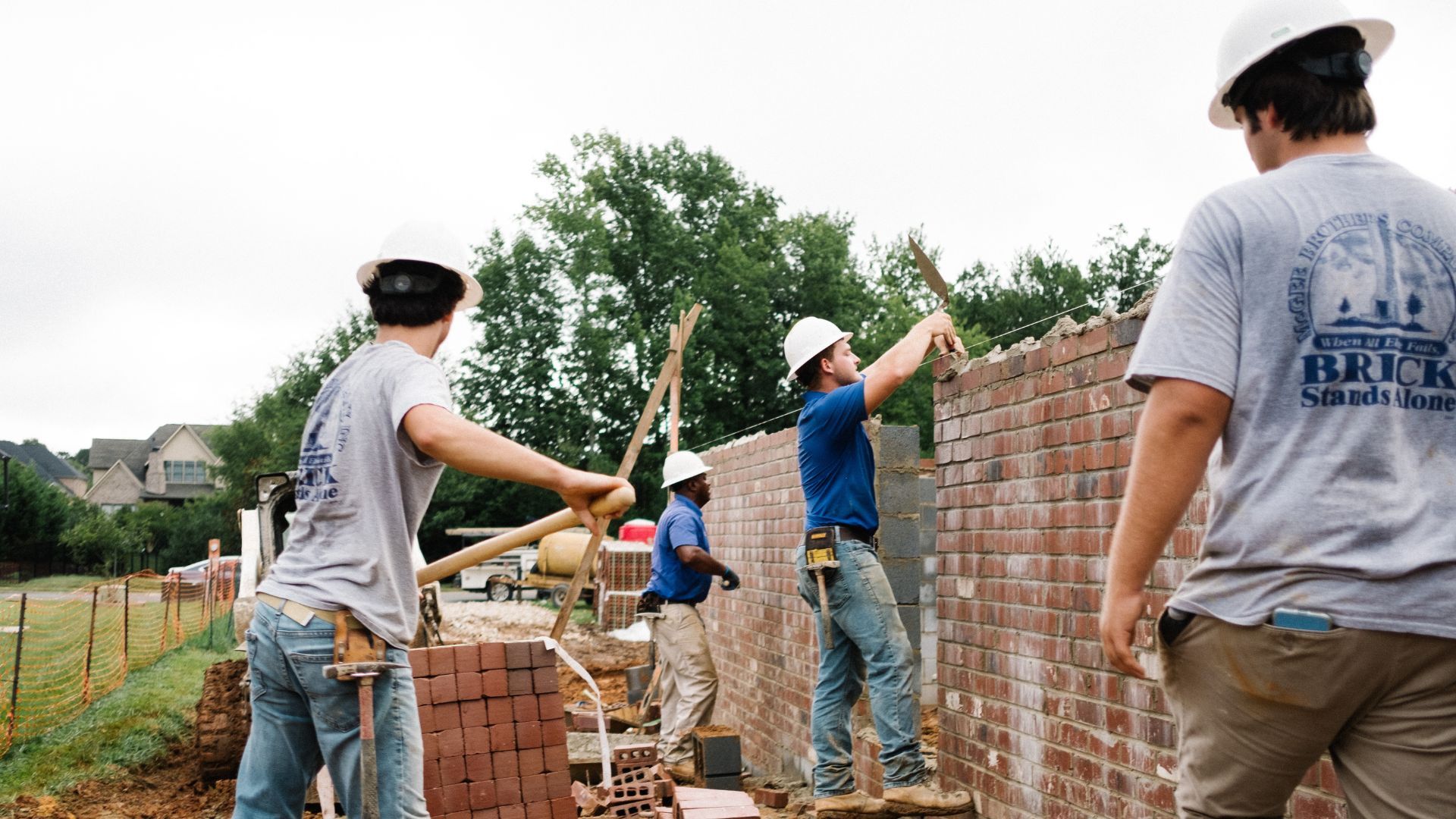 Four men laying bricks on a wall at a construction site.