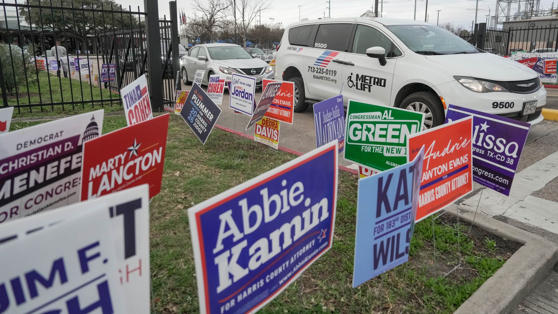 A Metro van drives out of a parking lot with political signs in the forefront
