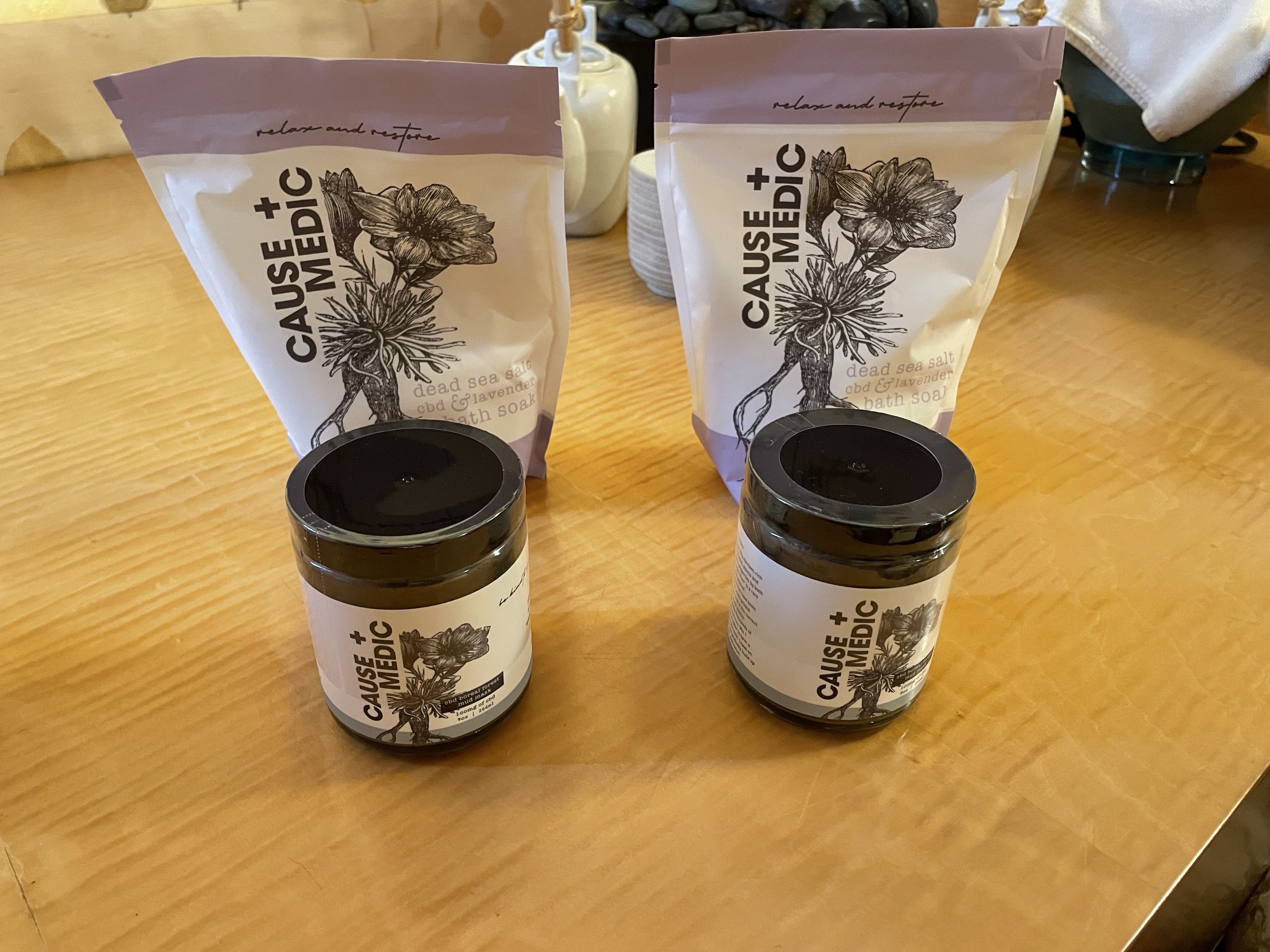 Two small containers are labeled "cbd boreal forest mud mask," and behind are two bags labeled dead sea salt cbd and lavender bath soak.