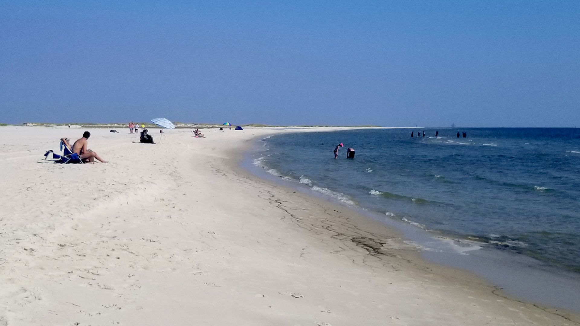 Beach-goers relax in the sun on Dauphin Island as a calm wave hits the sandy shore.