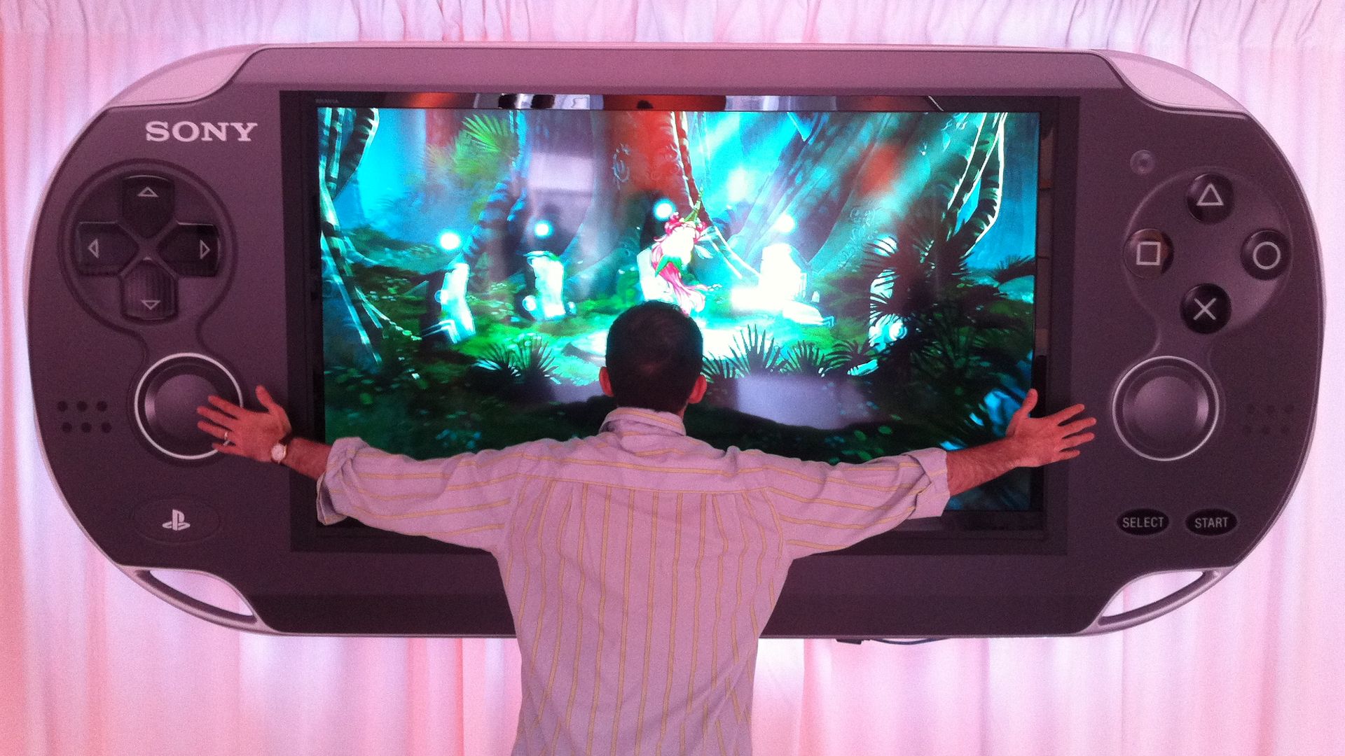 Photo of a man seen from behind, arms outstretched across a giant version of a portable gaming device hanging from a wall