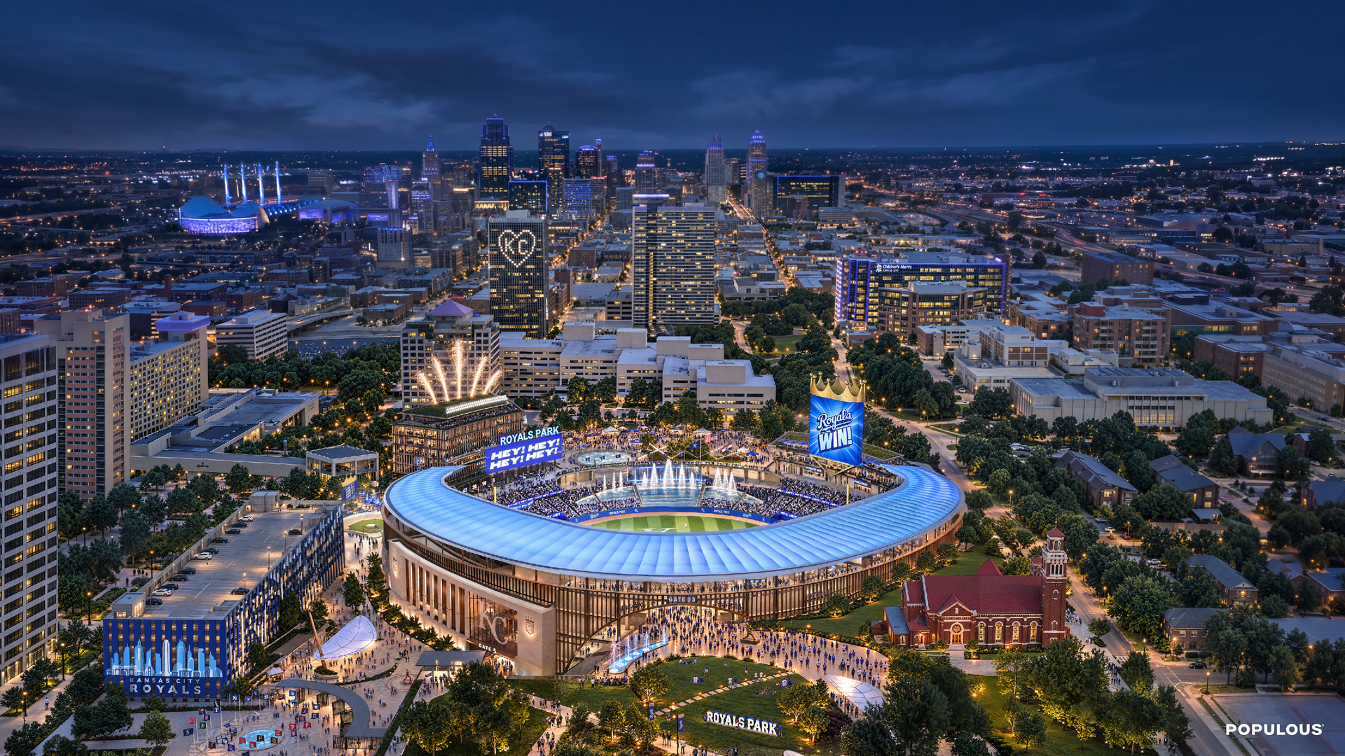Aerial night view of downtown Kansas City featuring a large blue-roof stadium labeled Royals Park in the foreground, illuminated skyscrapers, and a heart-shaped light on a building.