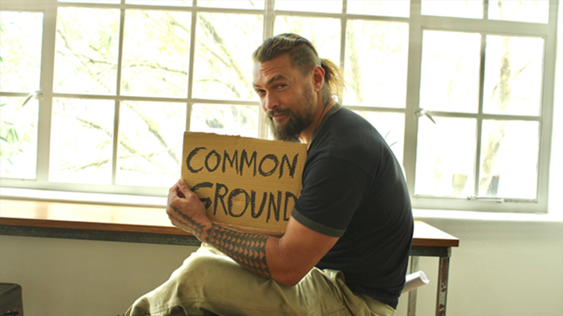 Photo of an actor holding a sign that says Common Ground 