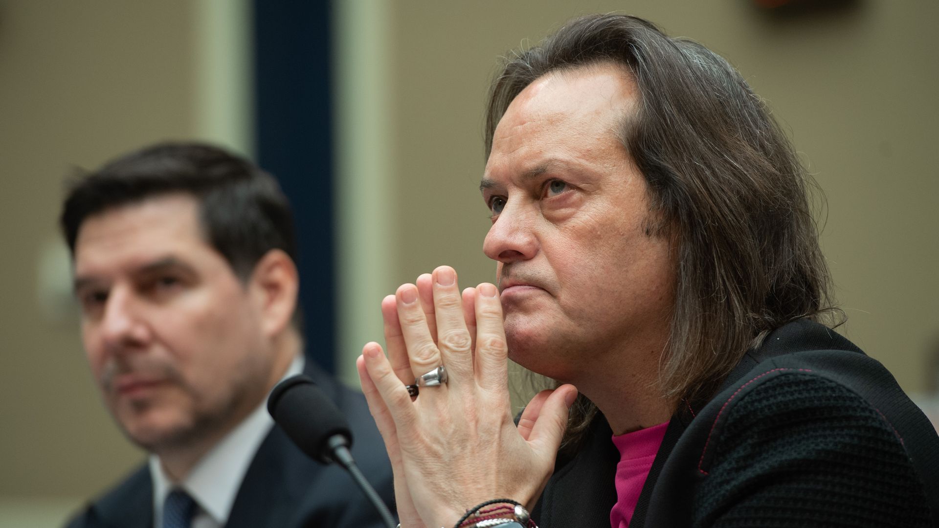 A man in profile looks forward, his hands clasped near his face