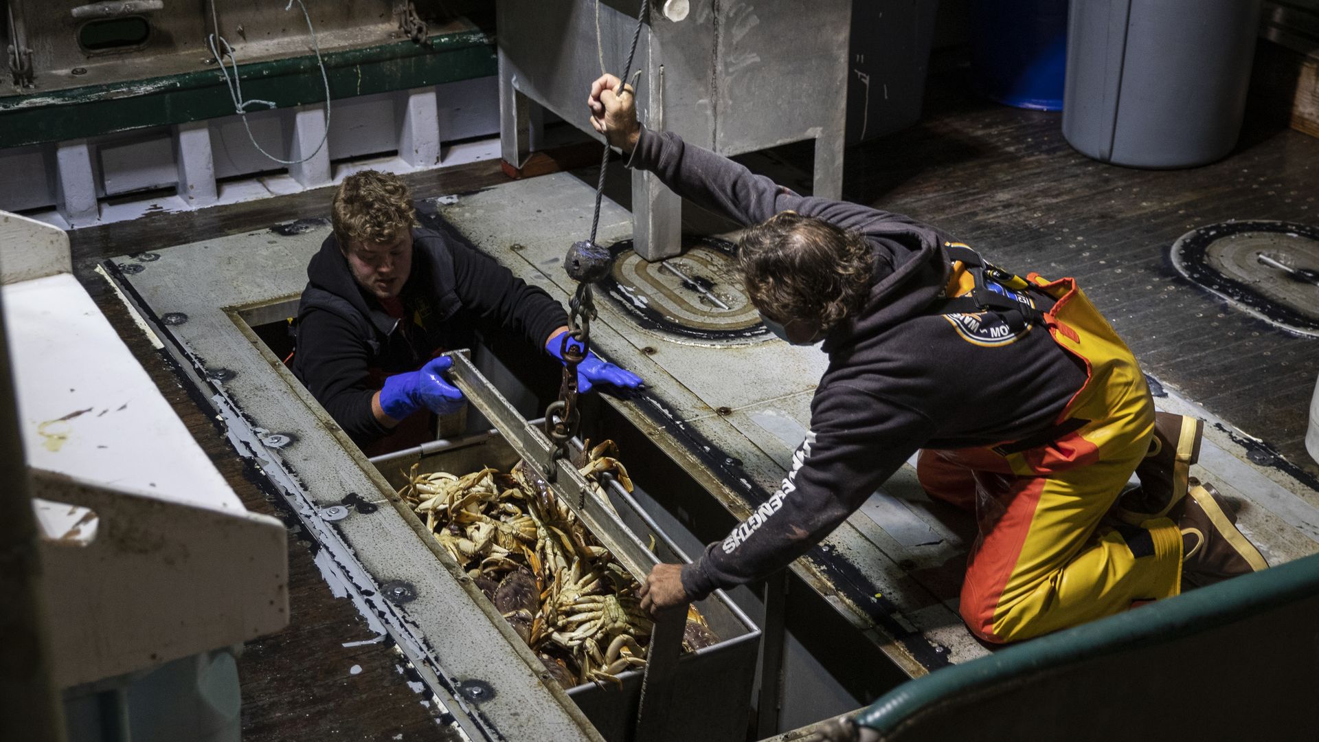 Commercial fisherman Bob Maharry, right, and deckhand Drake Hoffman guide a basket of Dungeness crabs on Pier 45 in San Francisco, California on March 18, 2021.