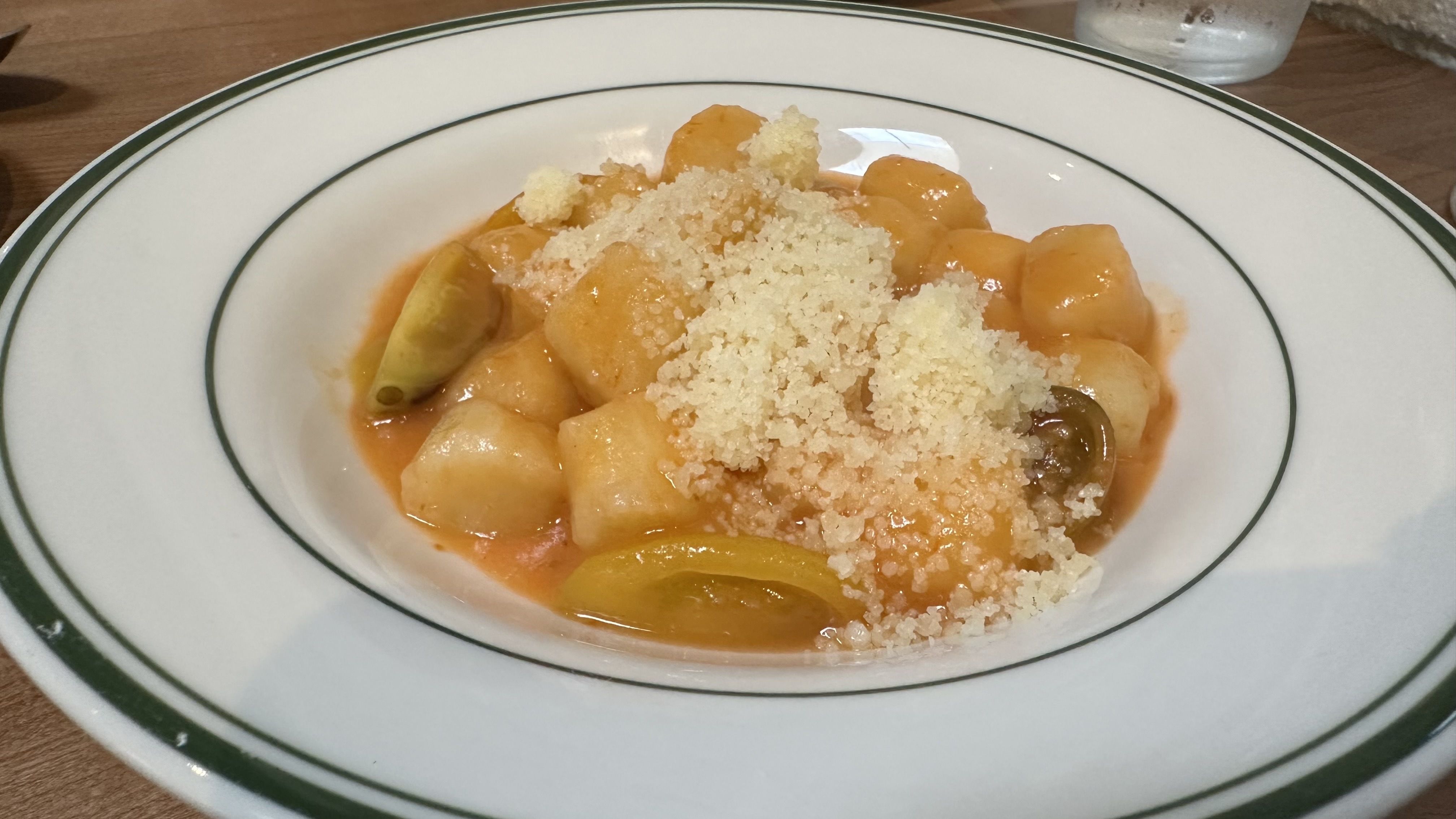 Gnocchi in tomato sauce, topped with cheese, served on a white plate with a green rim.
