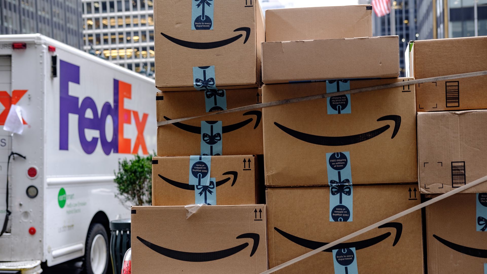 Amazon boxes sit on top of each other alongside a white FedEx truck.