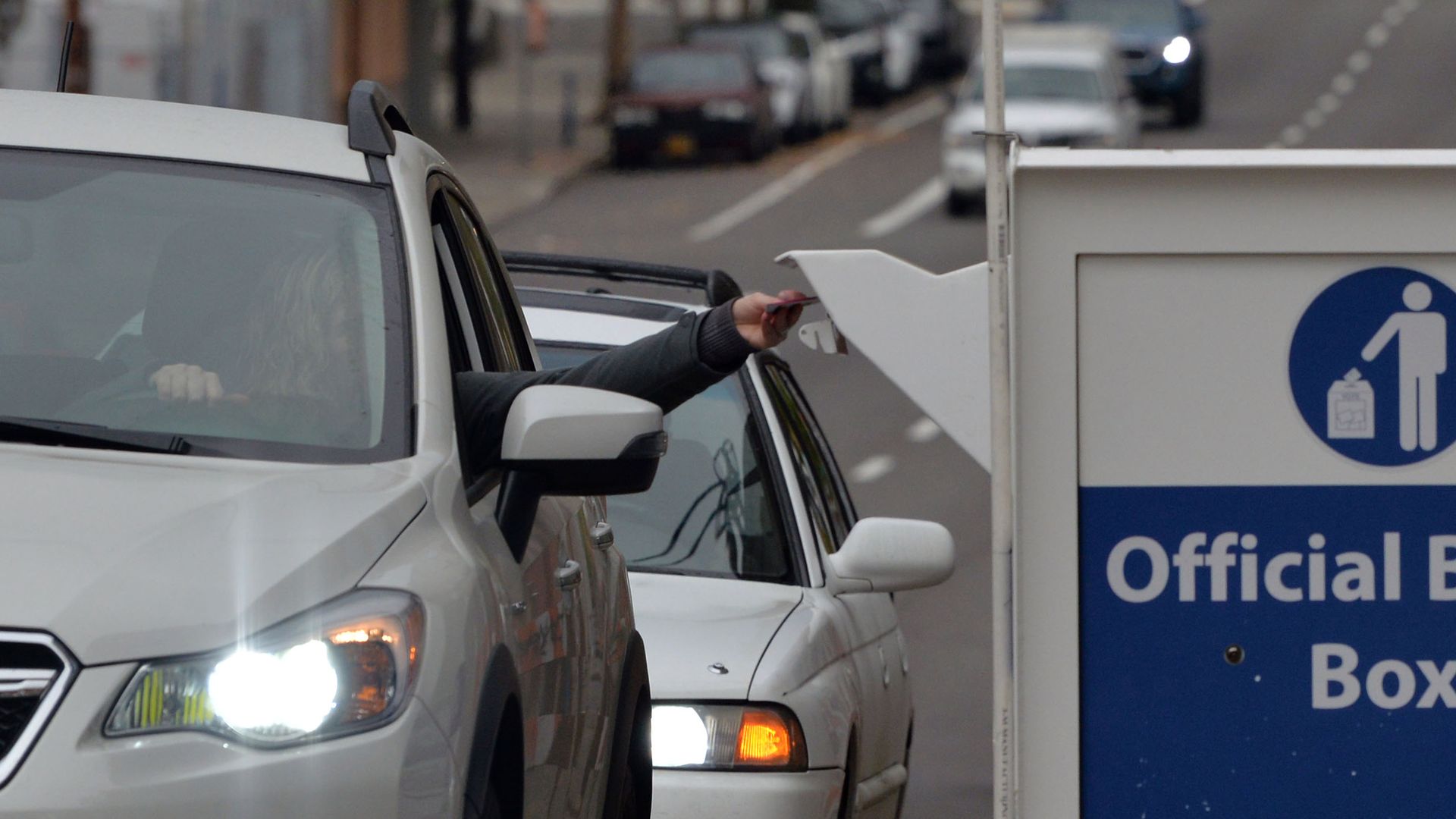 A voter leans out of a car window to deposit a ballot into a drop box.
