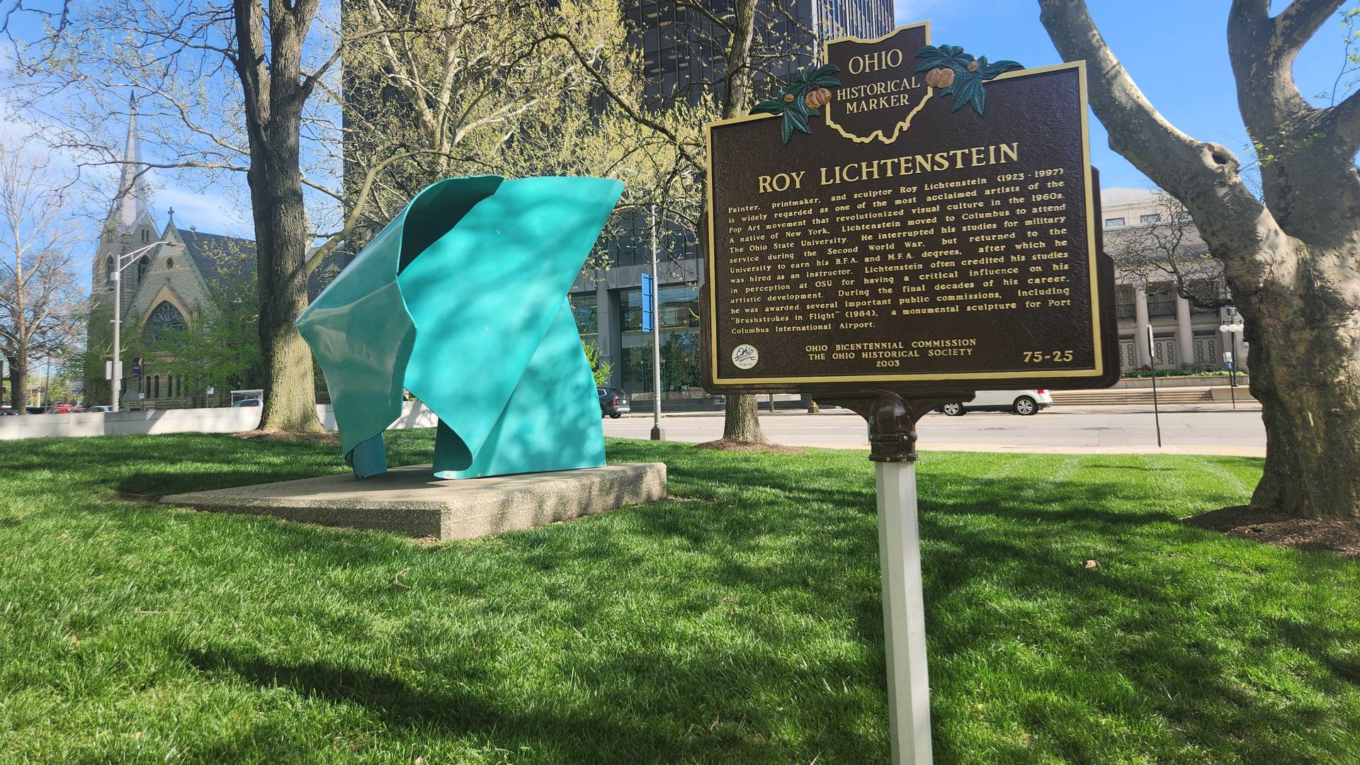 A historical marker for "Roy Lichtenstein" next to an outdoor sculpture. 