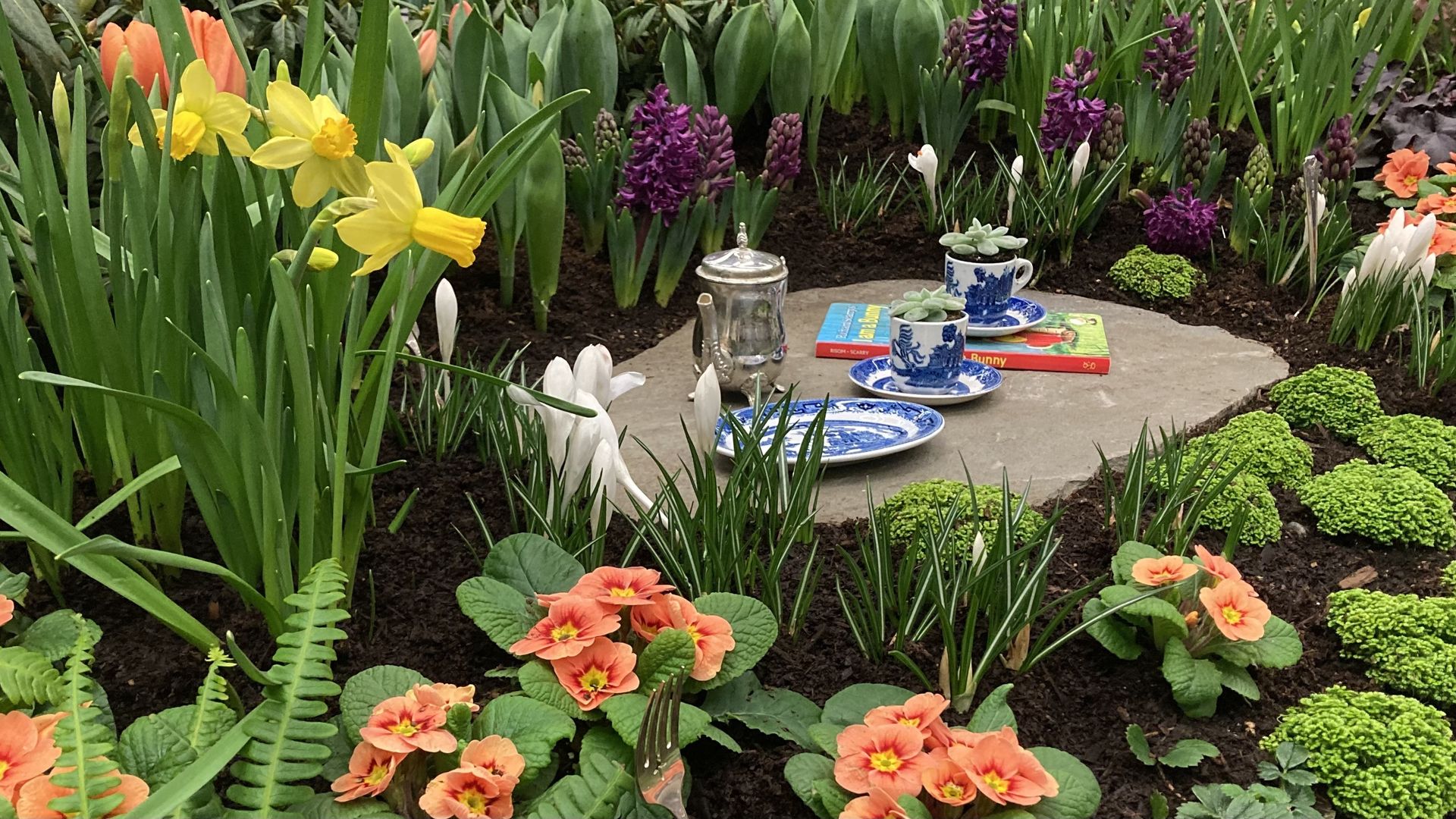 A photo of blooming flowers and a tea set on table in the middle.