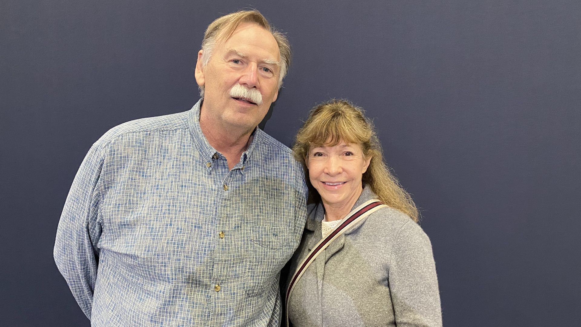 A man and woman standing next to each other in front of a gray background