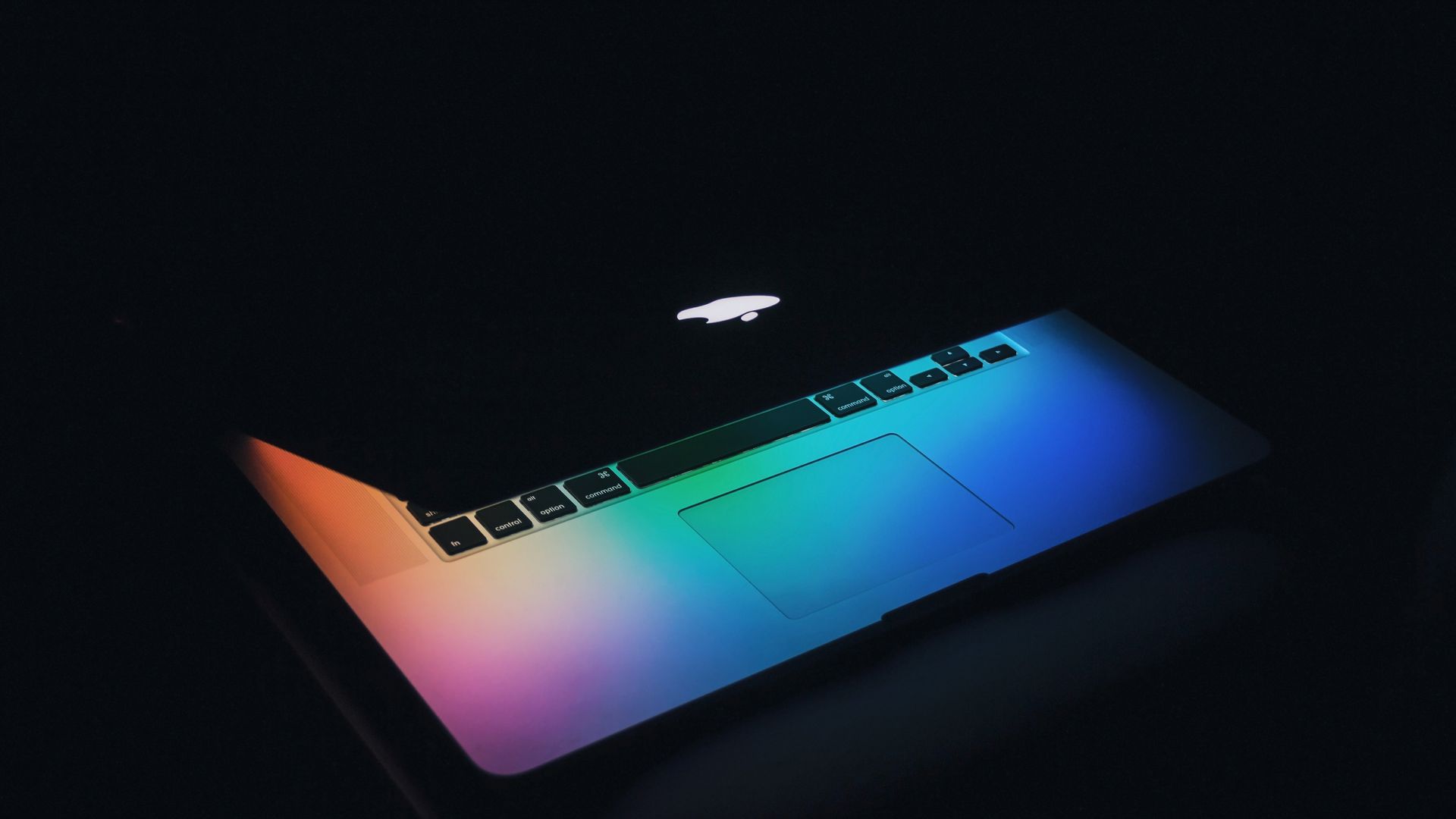 The partially closed screen of an Apple laptop glows rainbow colors