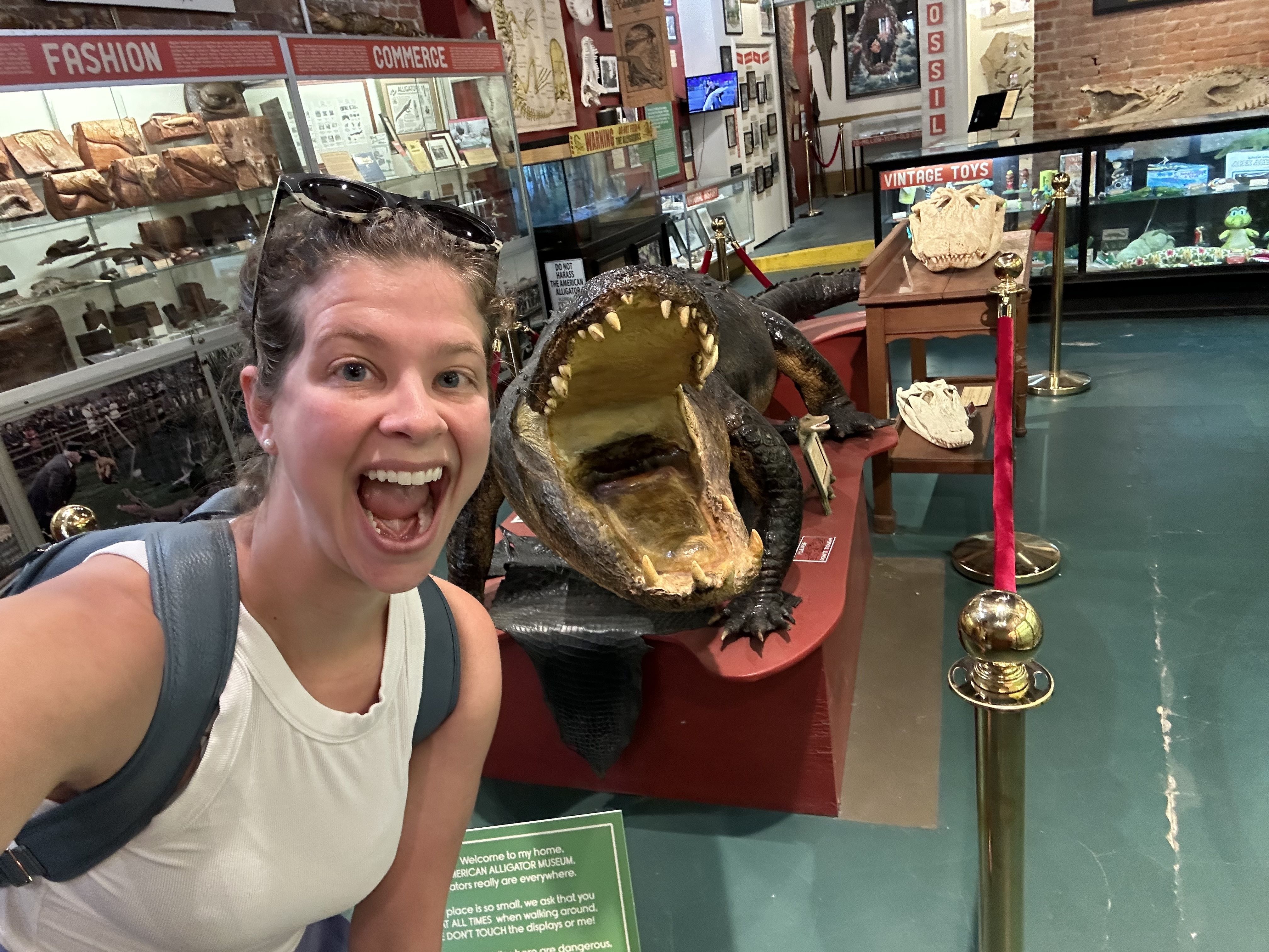 Chelsea Brasted poses, open mouthed, for a selfie next to a taxidermy alligator, which also has a wide open mouth.
