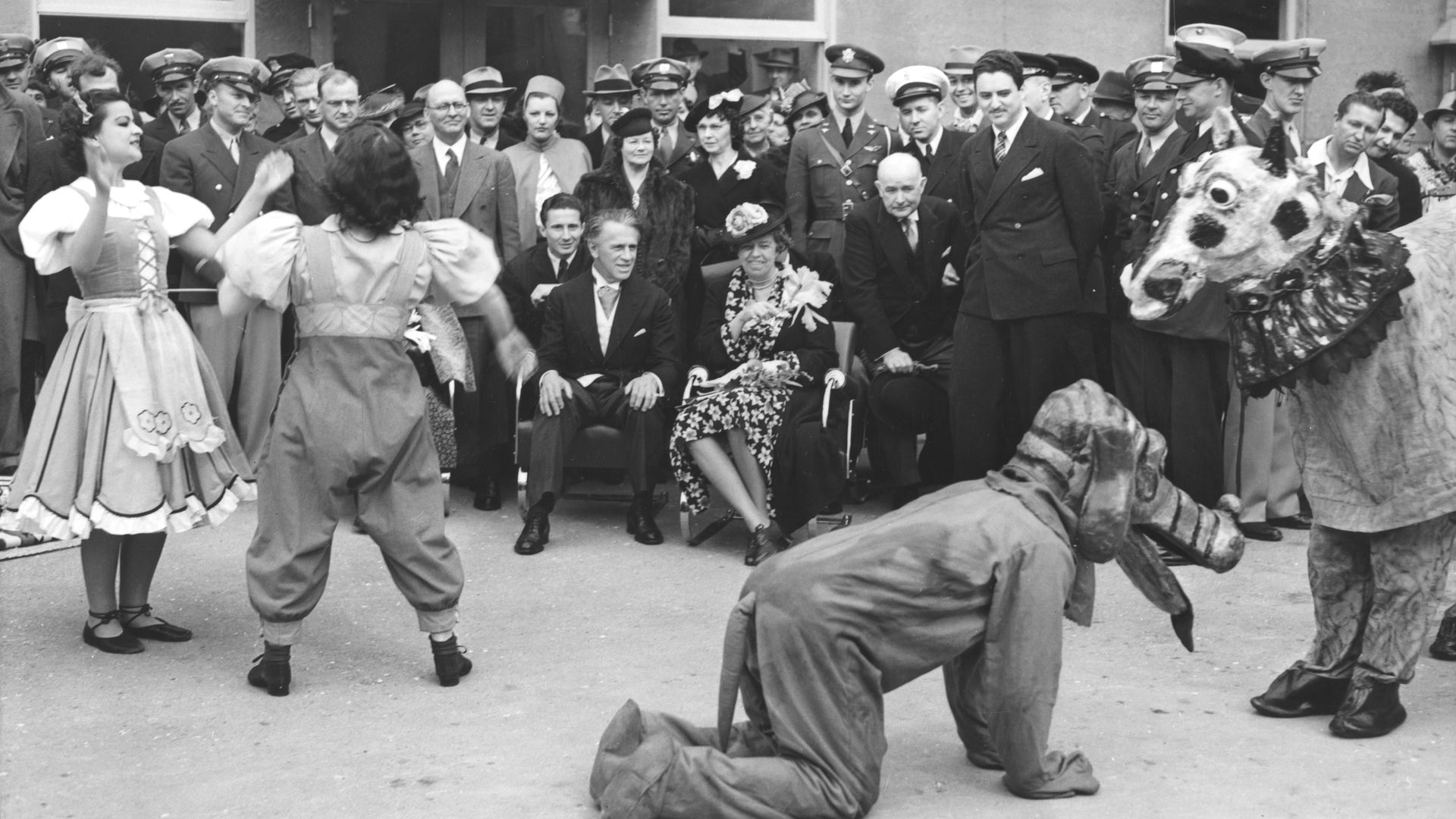 Photo of Eleanor Roosevelt sitting as she watches actors in costume perform a scene