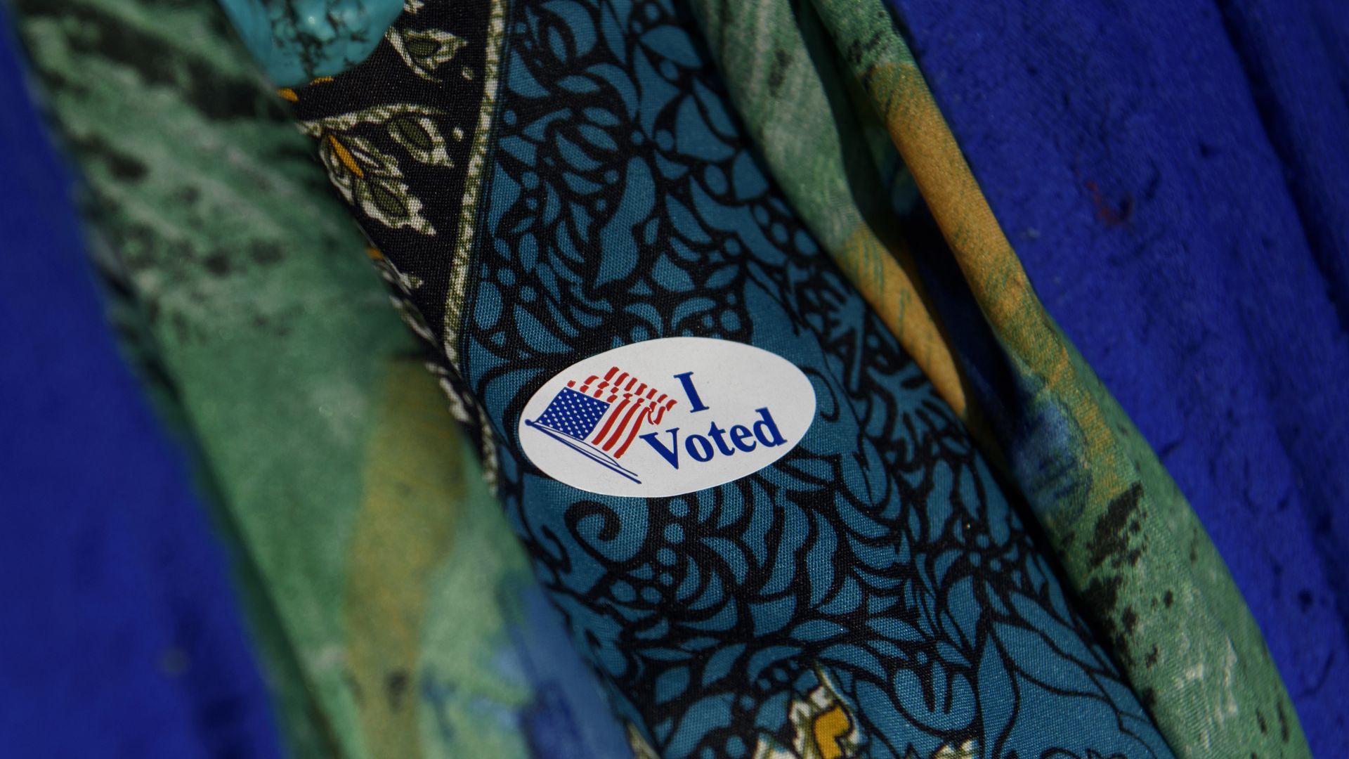 A close shot of a person wearing a blue and green top sports an "I Voted" sticker
