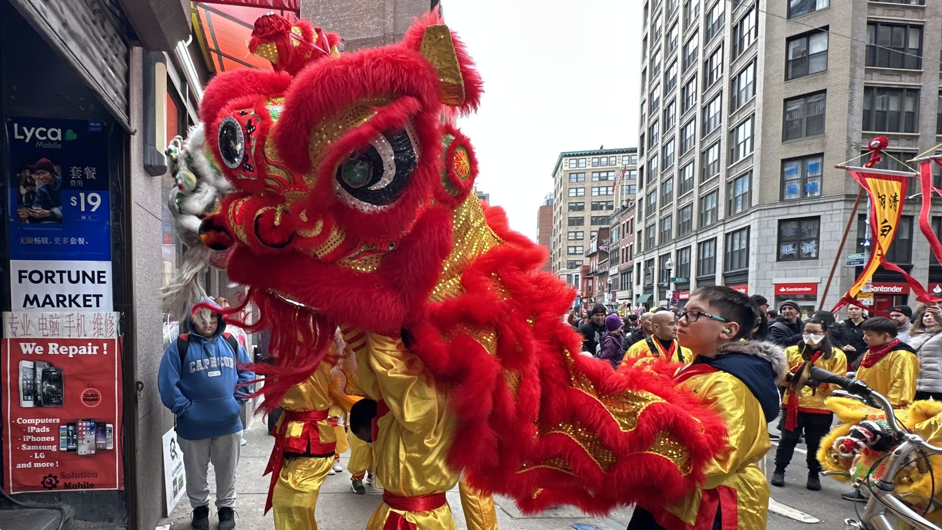 Two dancers stand in a red and gold lion and dance outside a local business in Boston’s Chinatown for Lunar New Year.