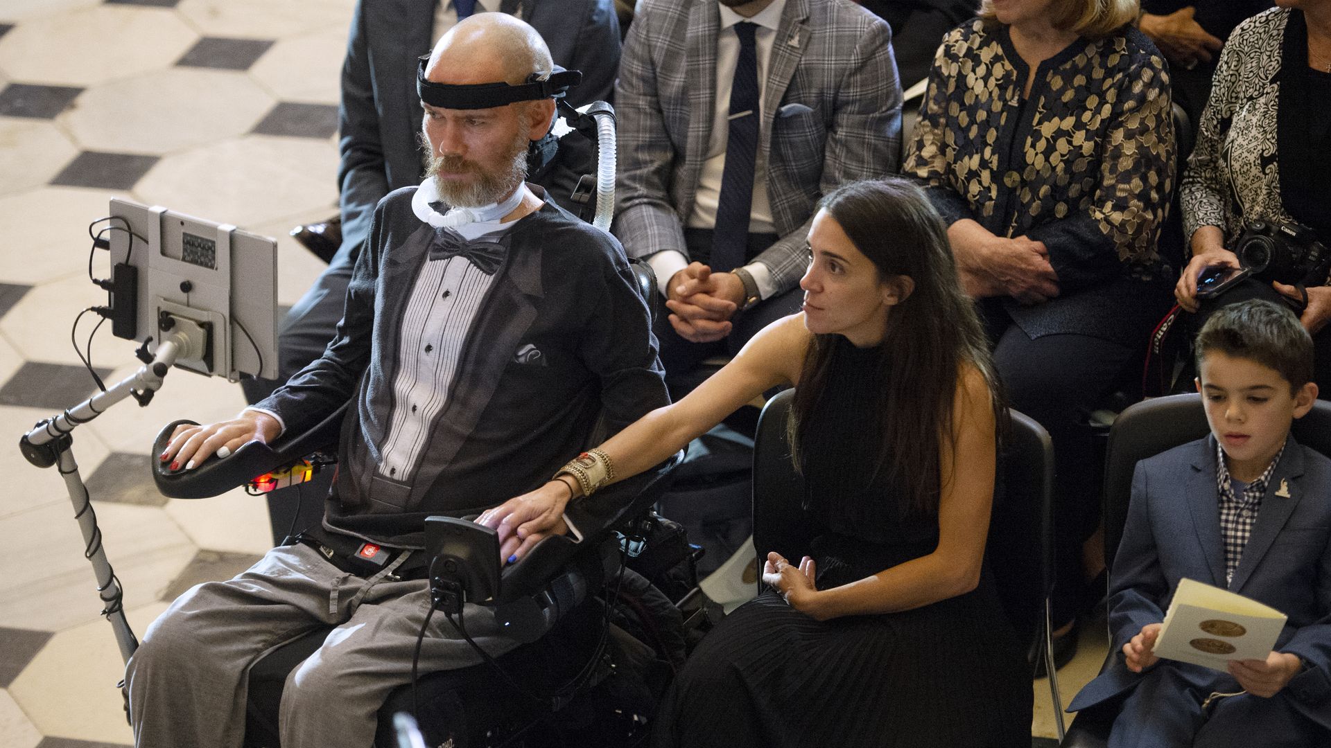 Steve Gleason sits in an audience while his wife, Michel Varisco Gleason, holds his hand. Their son sits next to her.