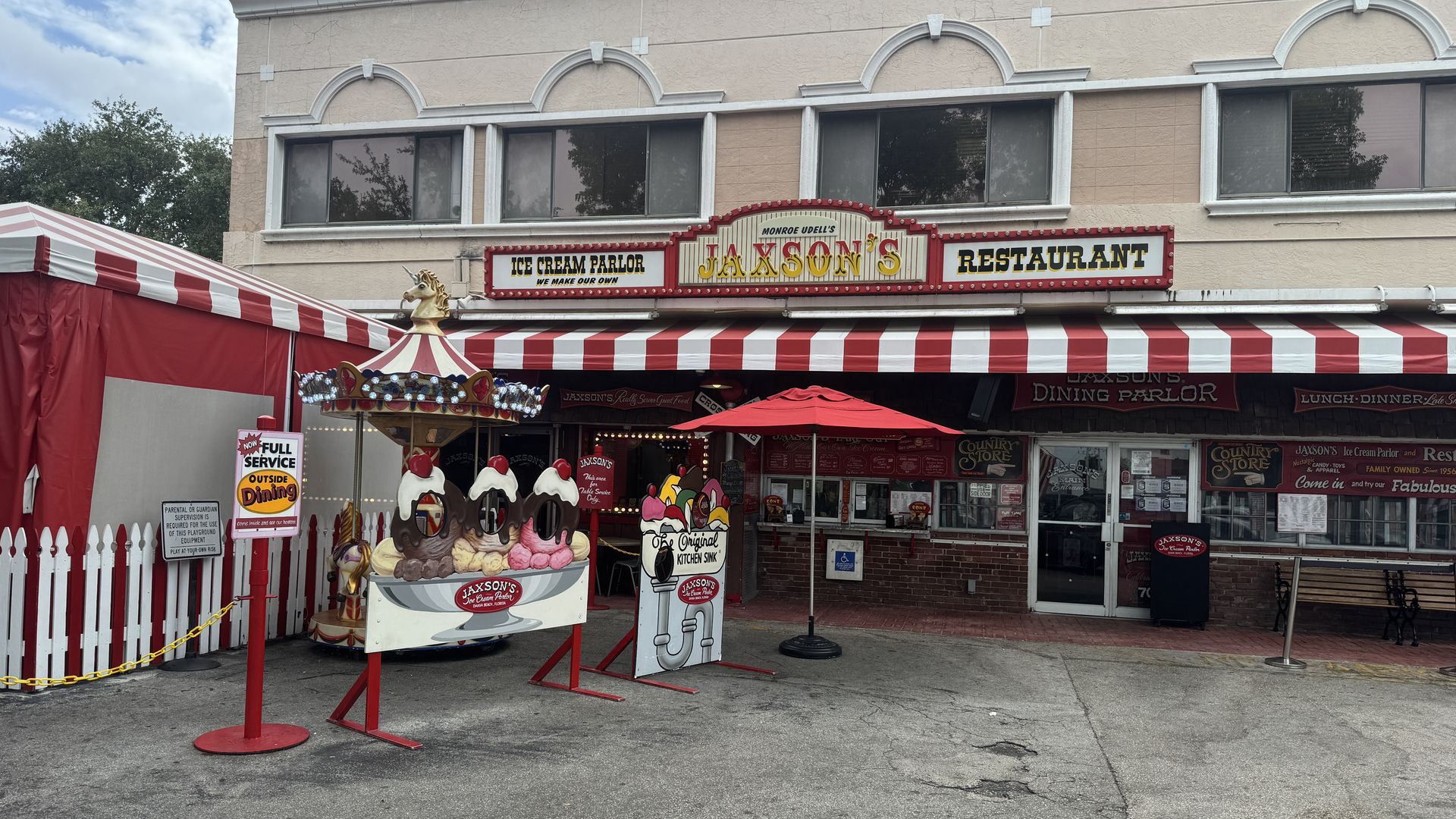Beige storefront with a red marquee reading "Jaxson's" Ice Cream Parlor & Restaurant; a red-and-white striped carnival tent in front, cartoon ice-cream cones, and a blue sky.