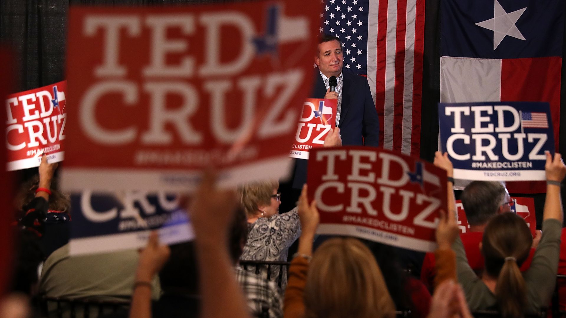Ted Cruz standing on stage at a rally in Texas, with a bunch of people holding Ted Cruz signs