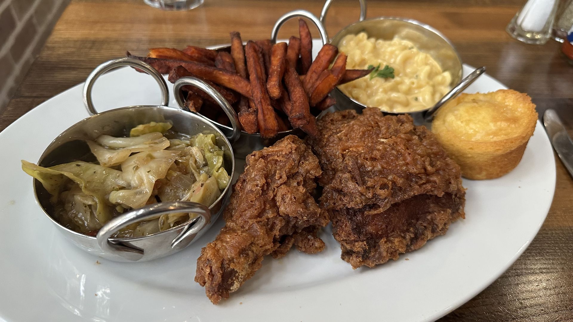A plate is covered with a fried chicken leg and thigh, a cornbread muffin, mac and cheese, sweet potato fries and cabbage.