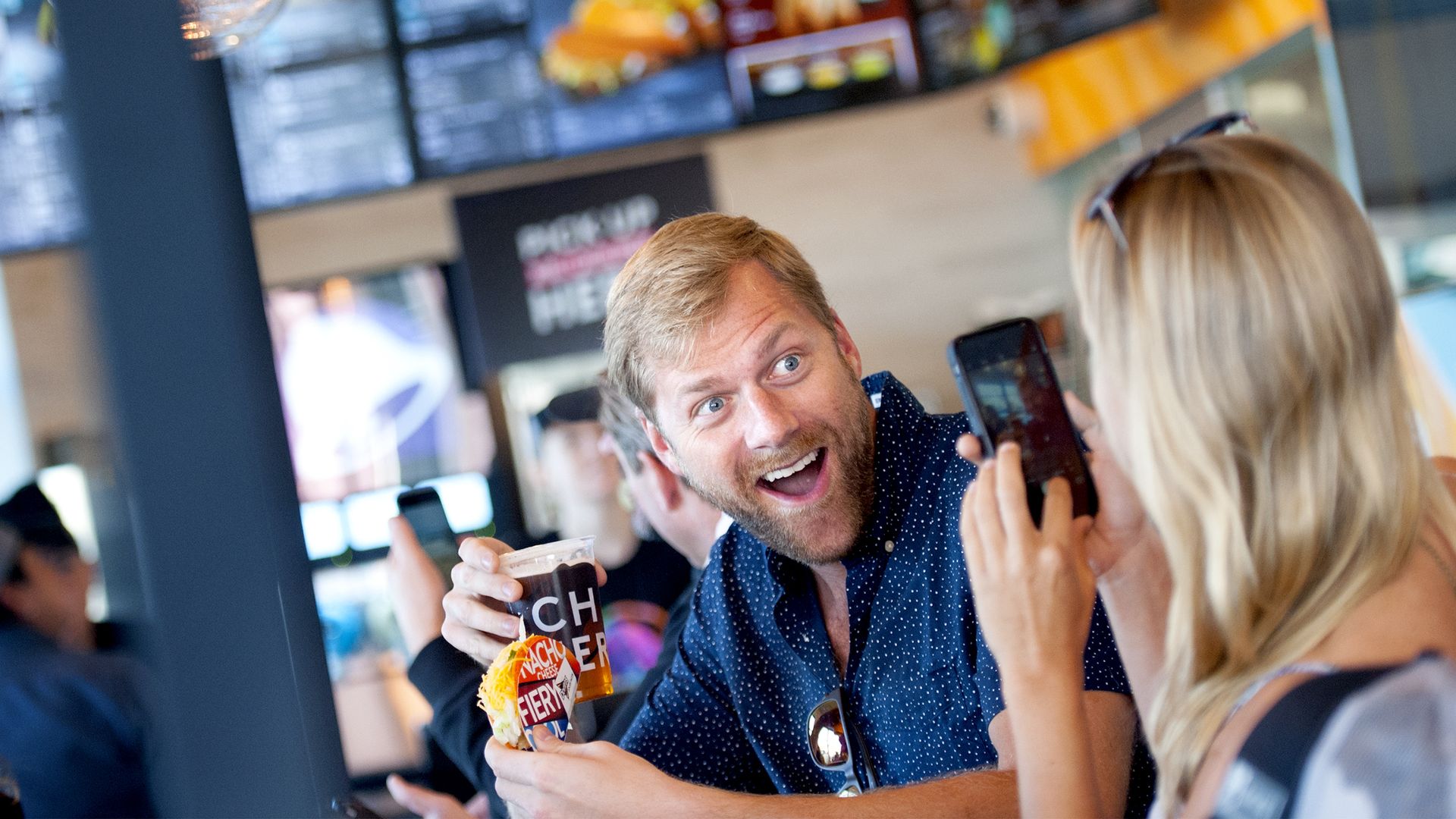 A man poses for a selfie with a drink and taco from Taco Bell Cantina, holding up the cup and smiling.