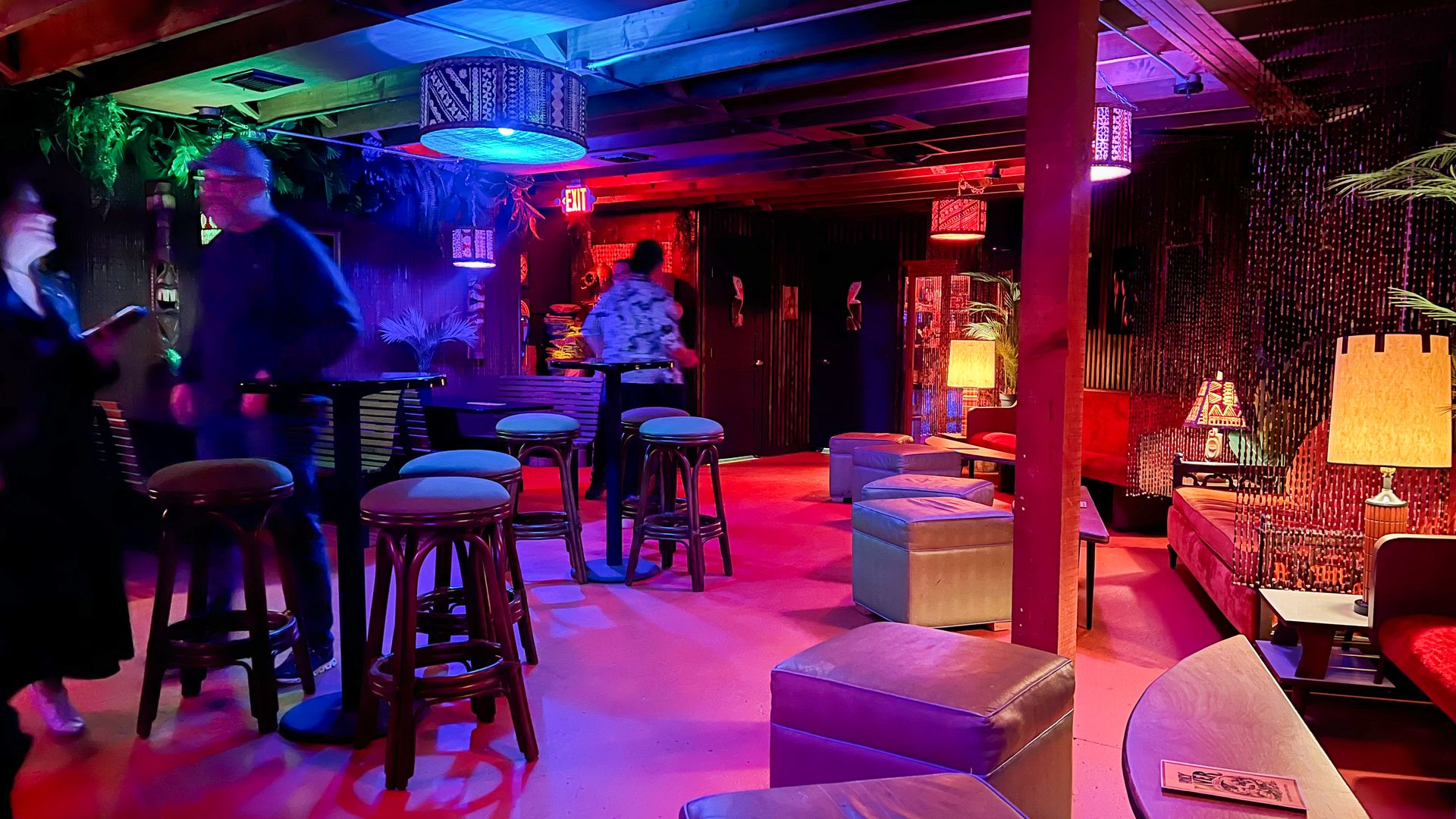 A small bar room with chairs and blue and pink mood lighting.