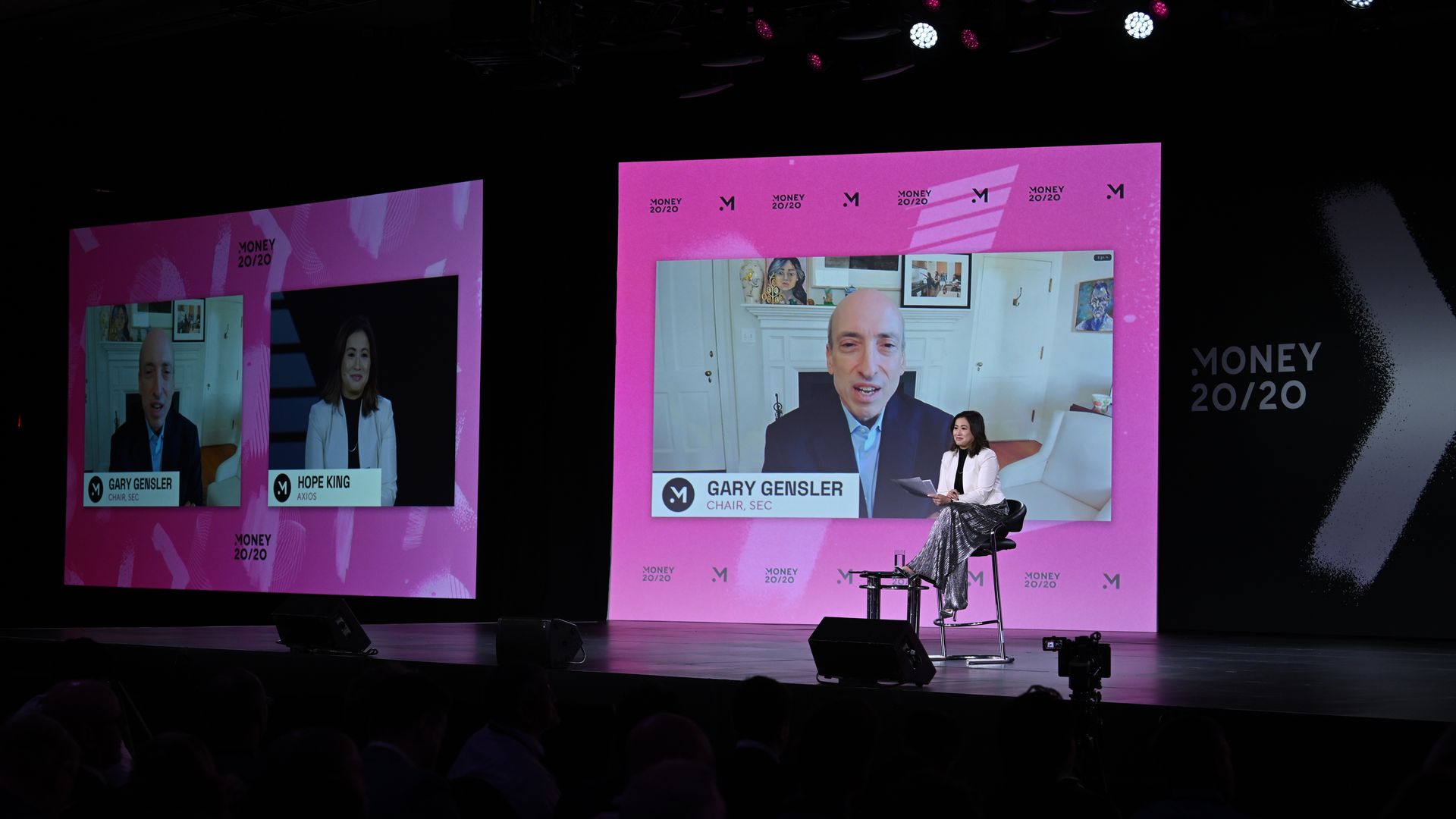 A person on stage, with a large screen behind featuring an interview subject.