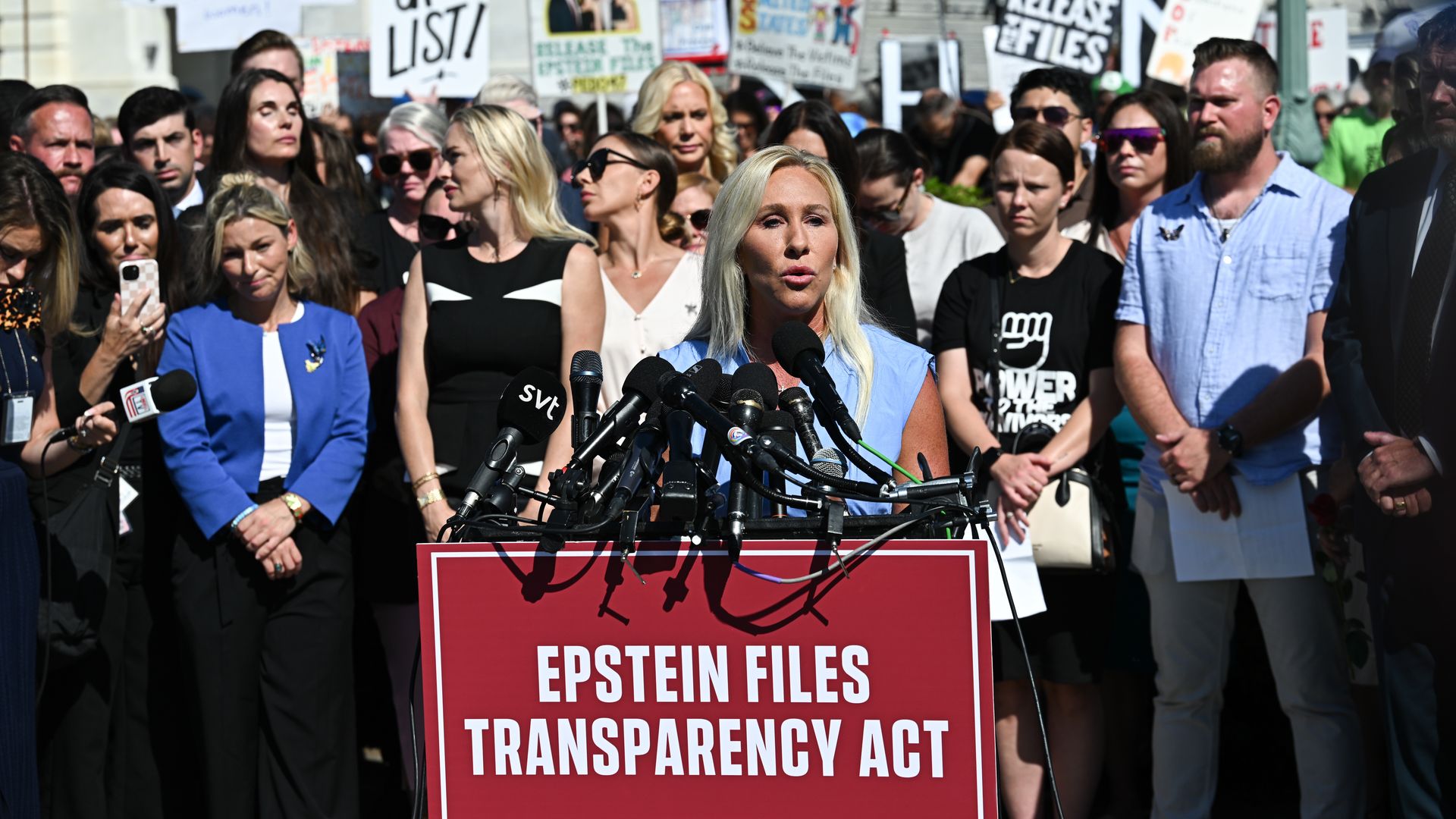 Marjorie Taylor Greene speaking at a podium with a sign that says "Epstein Files Transparency Act"