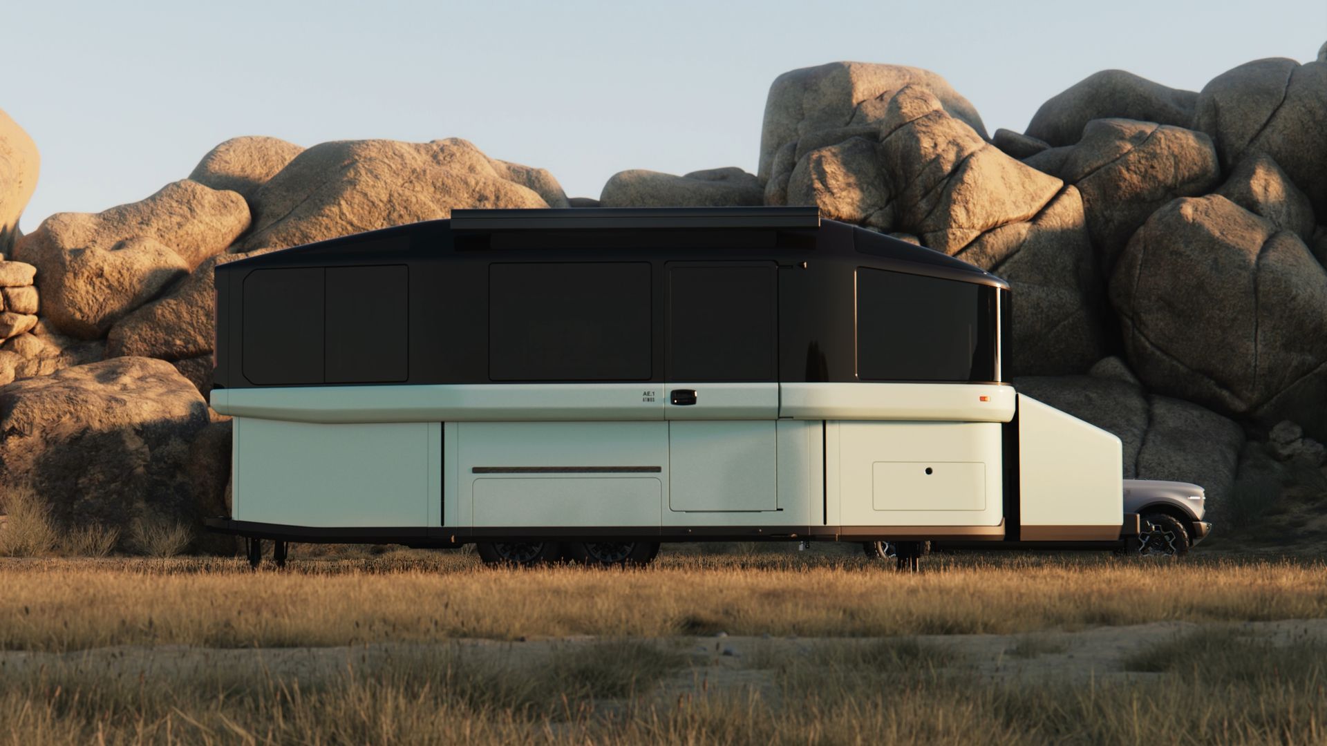 Large, futuristic luxury motorhome with a black upper cabin and white lower body rests on dry grass, set against rugged desert rocks at sunset; a pickup-like cab is visible on the right.